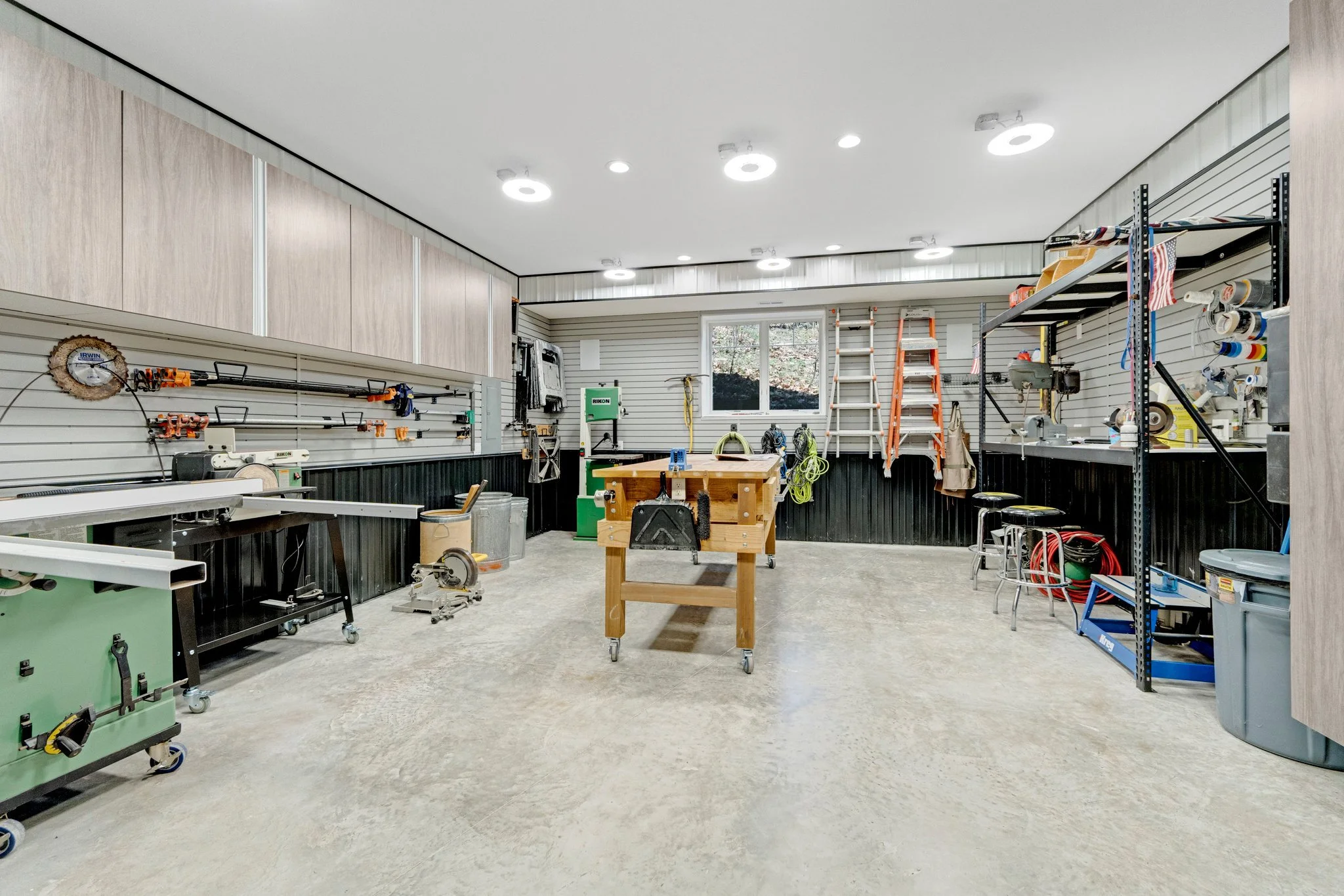 A spacious organized workshop with pegboard walls holding tools, a workbench, ladders, storage shelves, and equipment for woodworking and home improvement projects.