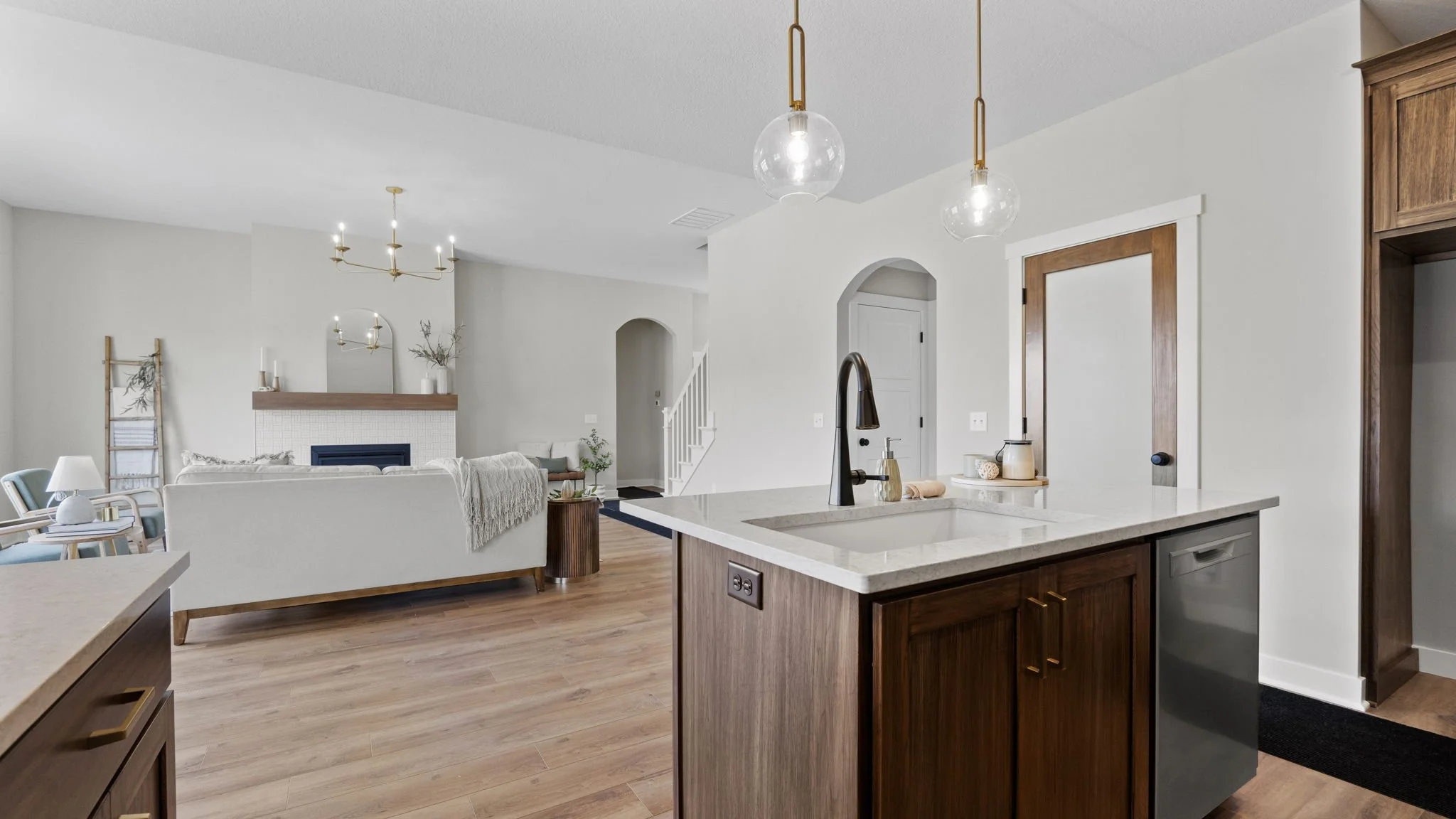 Open-concept living room and kitchen with modern decor, hardwood floors, pendant lights, a fireplace, and minimalist furniture.