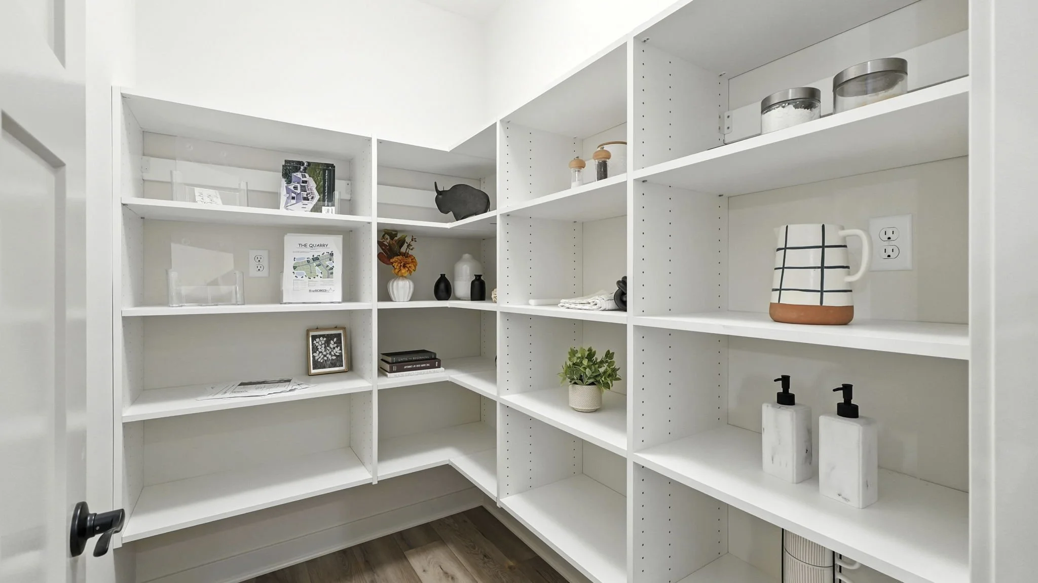Empty white shelving unit in a room with various decorative items and small potted plants.