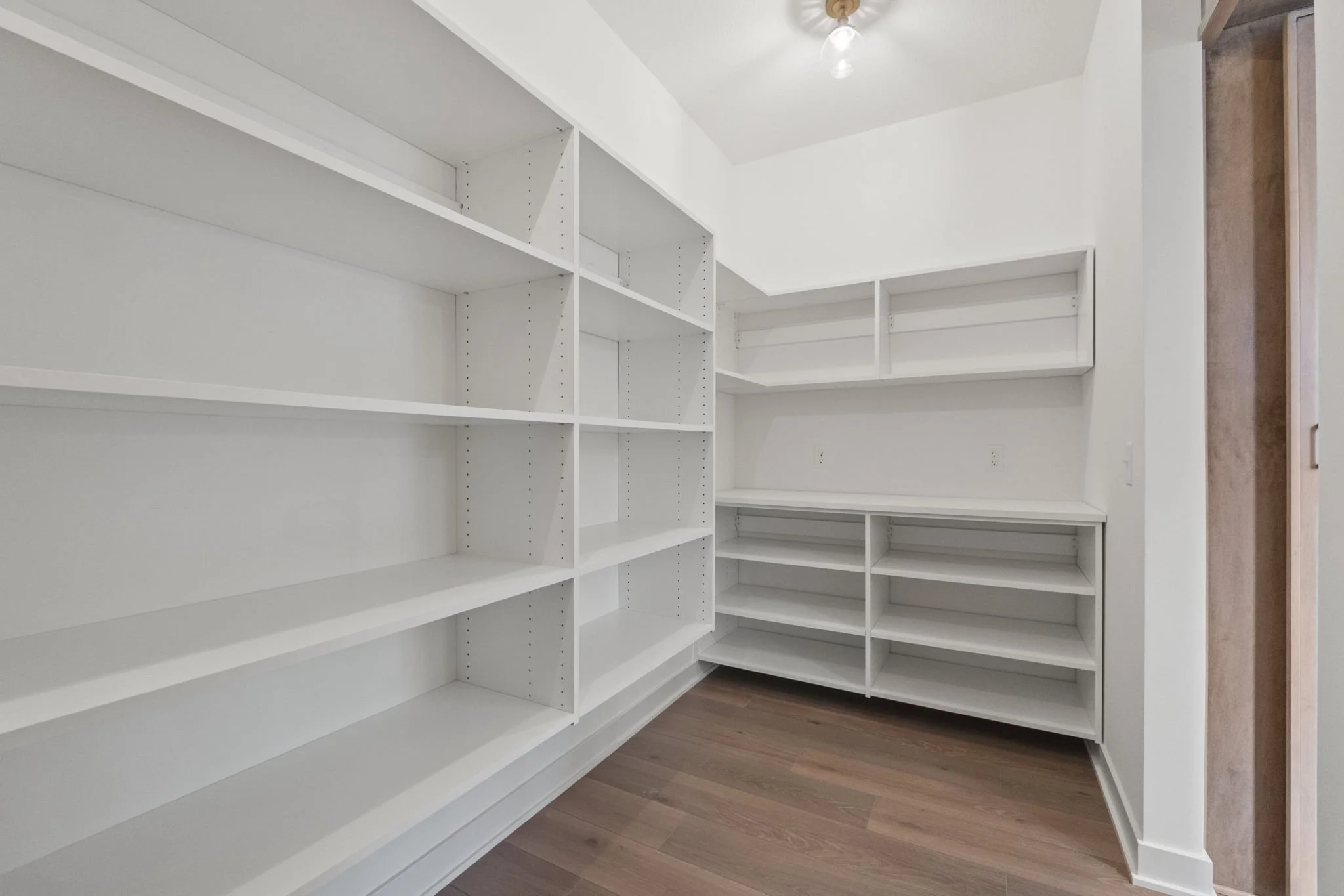 Empty white built-in shelves and cabinets in a pantry or closet with wood flooring.