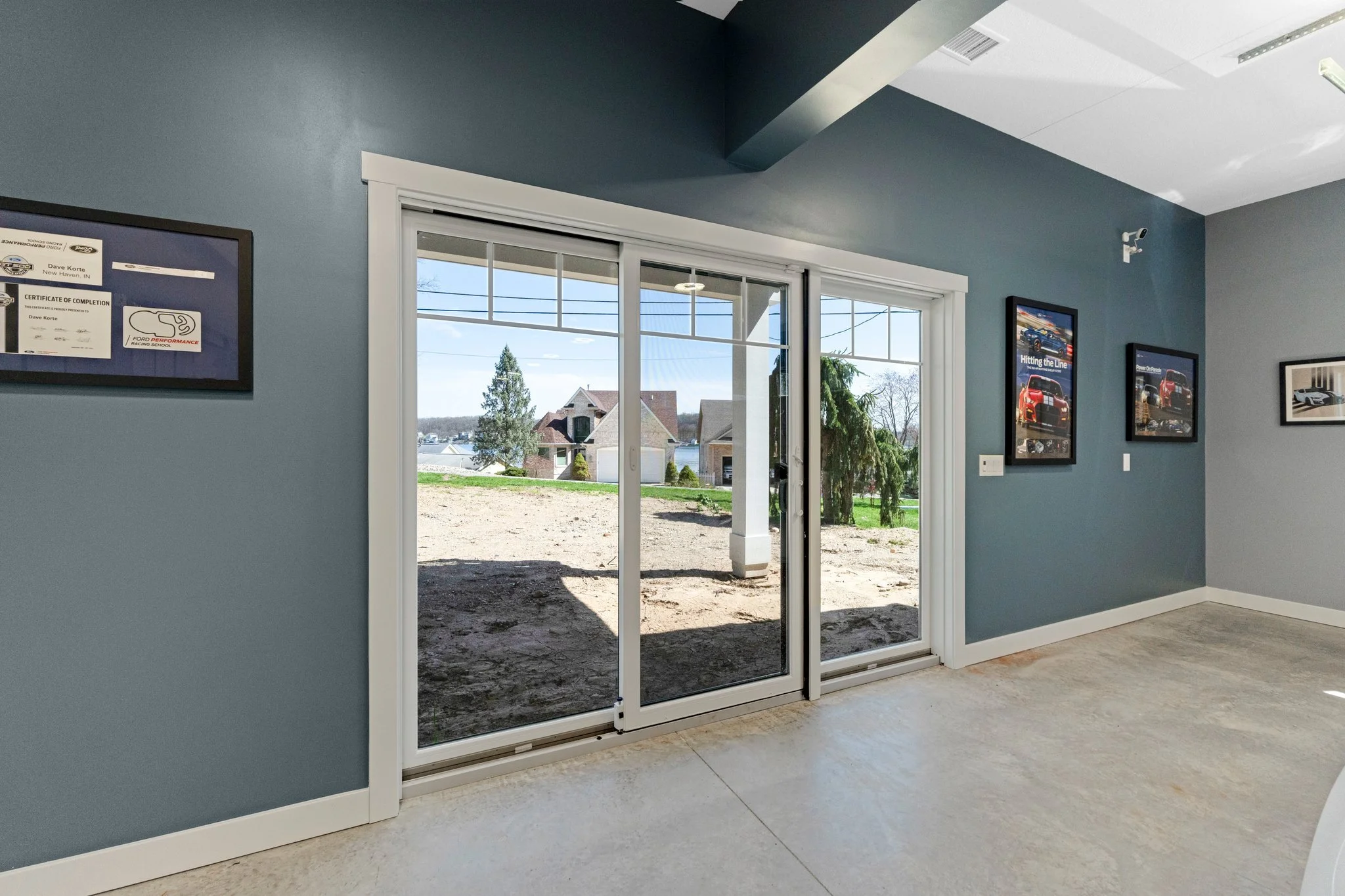 Interior view of a room with blue walls and a sliding glass door leading outside, showing a yard and neighboring houses.