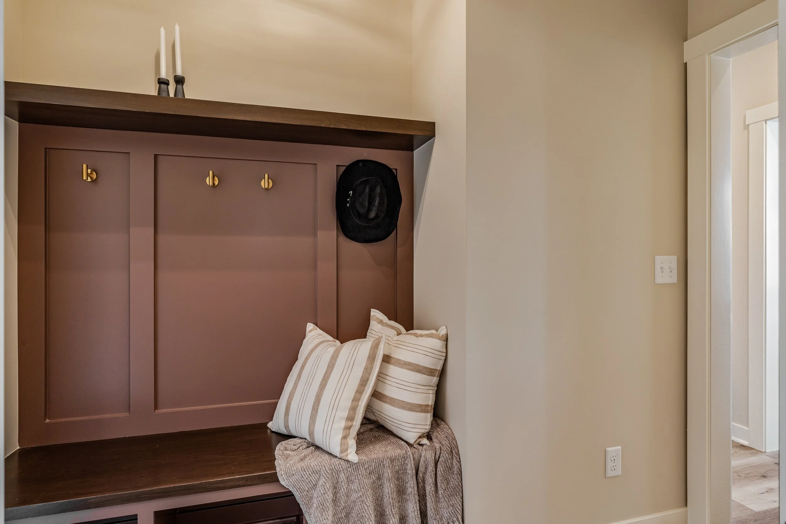 Interior wall corner with a built-in bench, leaning pillows, and a hat hanging on gold hooks.