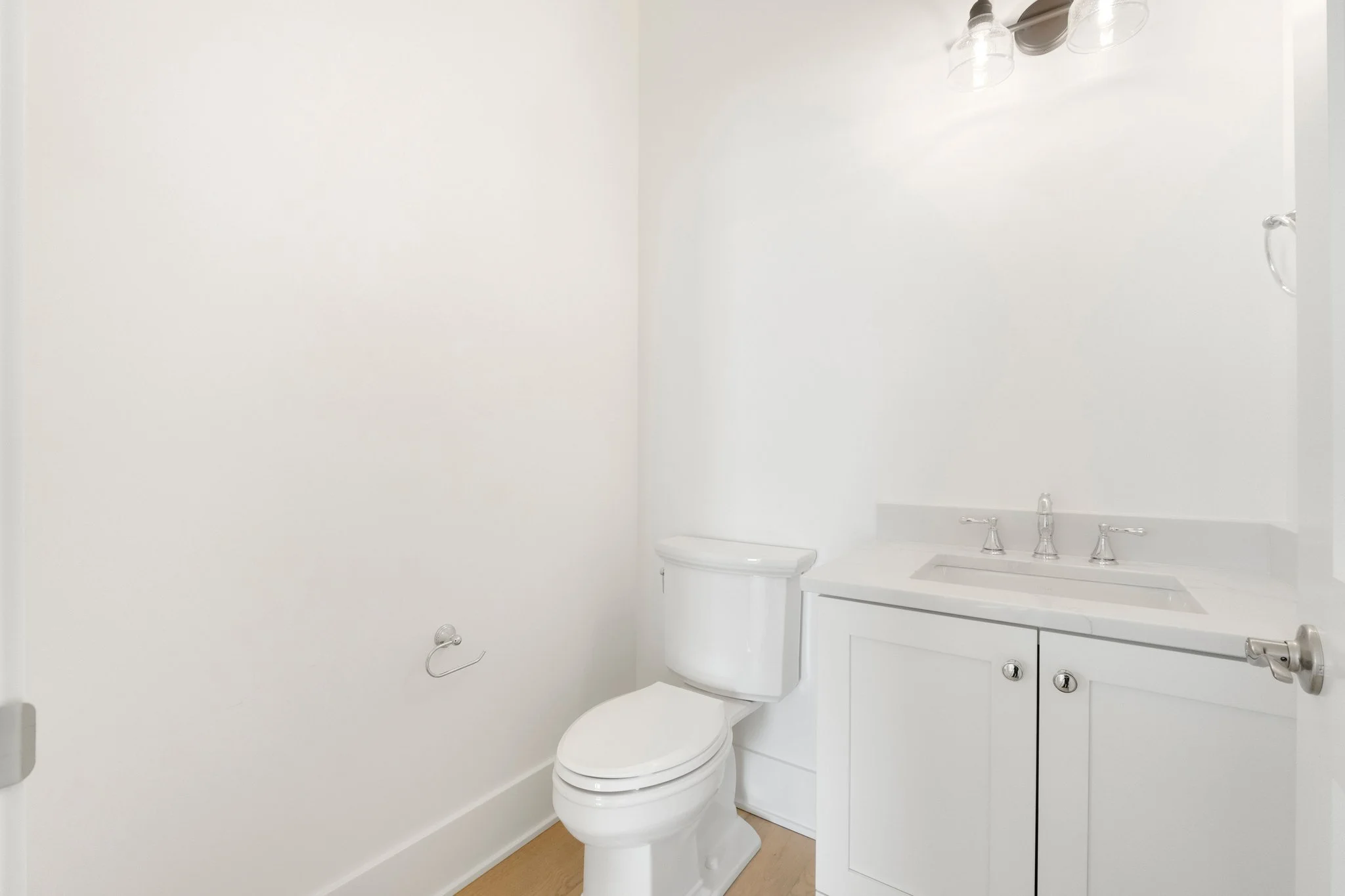 A small, white bathroom with a toilet, a white vanity with a sink, and a mirrored light fixture.