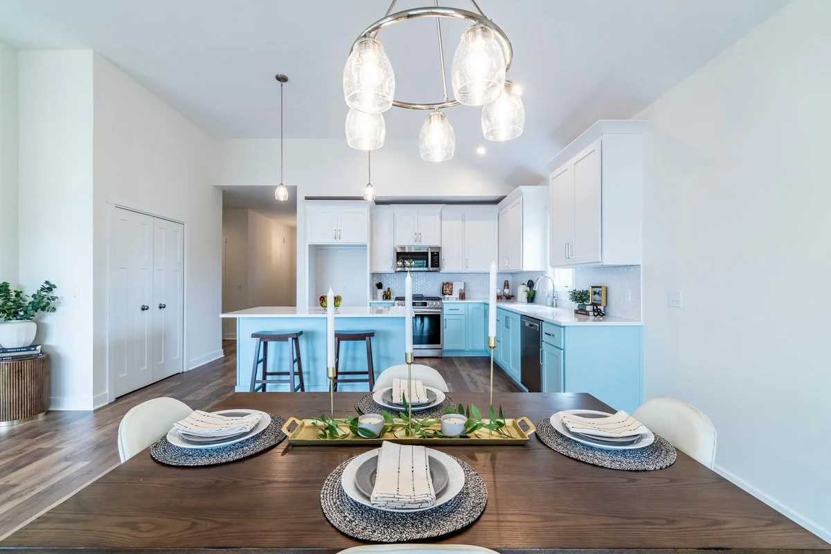 Modern kitchen and dining area with white and light blue cabinets, wooden dining table set for four, and a contemporary light fixture.