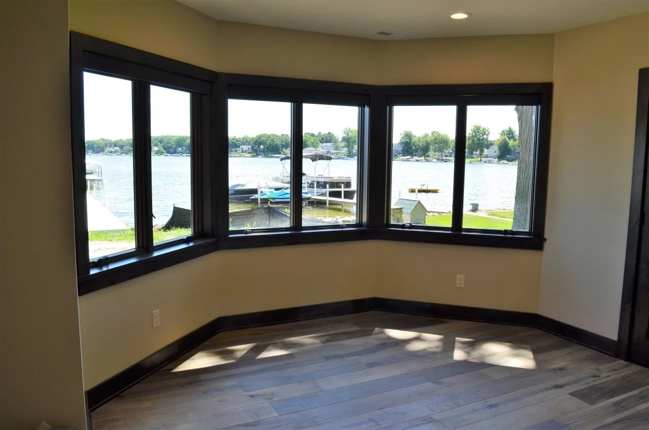 Interior of a room with large bay windows overlooking a lake with boats and greenery.