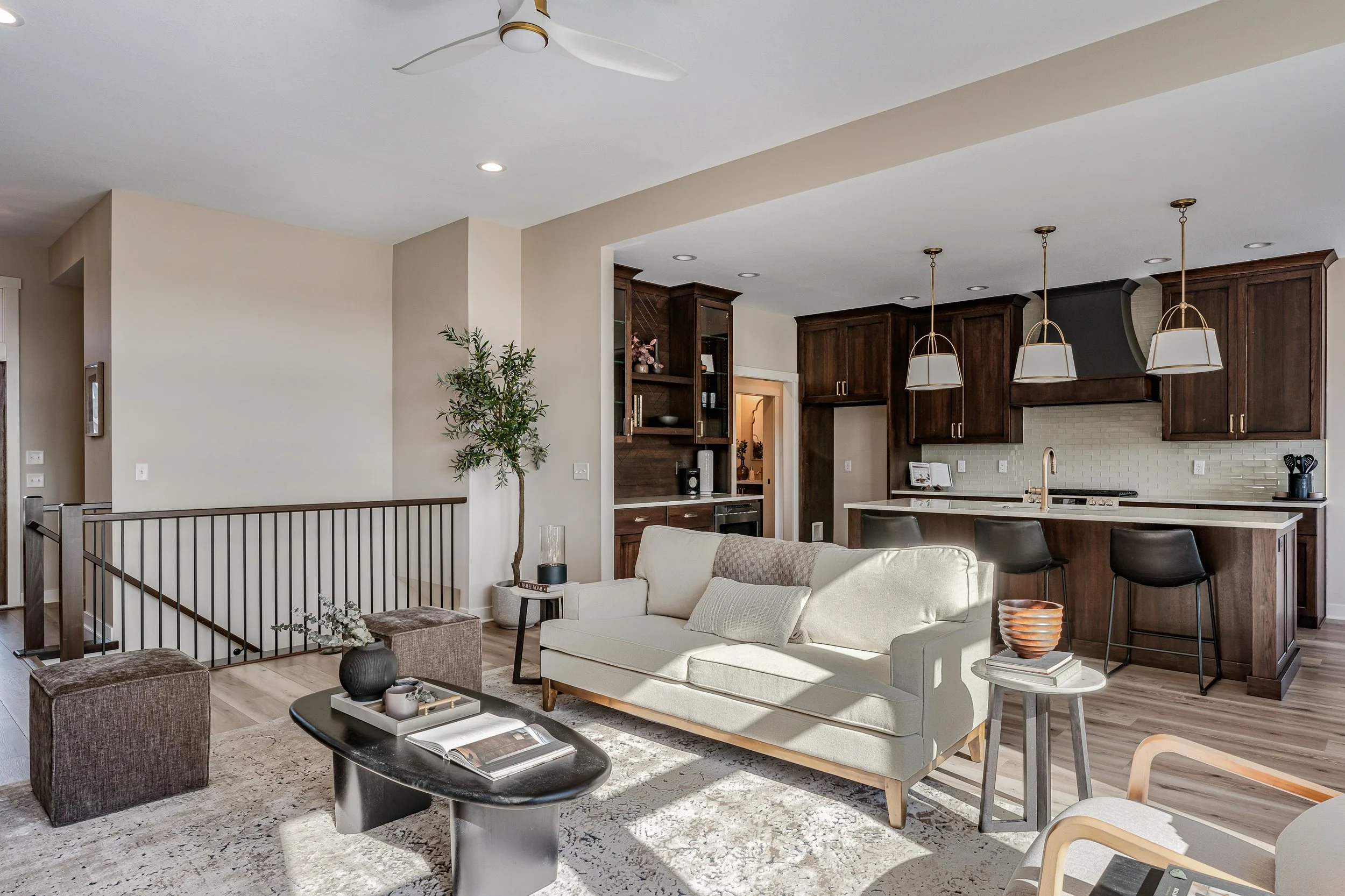 Open-concept living room and kitchen in a modern home with beige walls, dark wood cabinets, white countertops, and pendant lighting over the kitchen island.