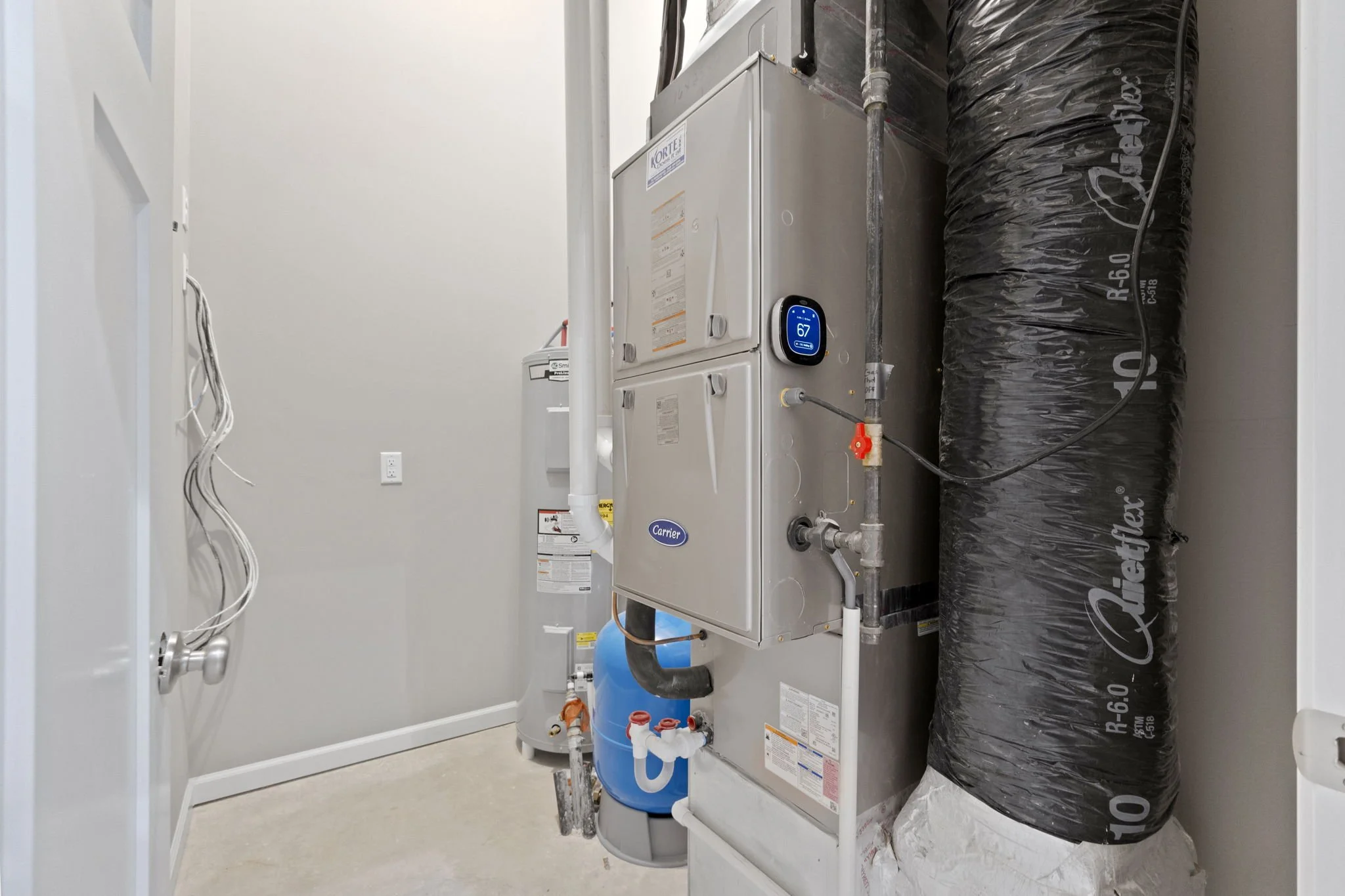Utility room with a white tank water heater, a black insulated vent pipe, and a furnace with a digital thermostat display showing 67 degrees.