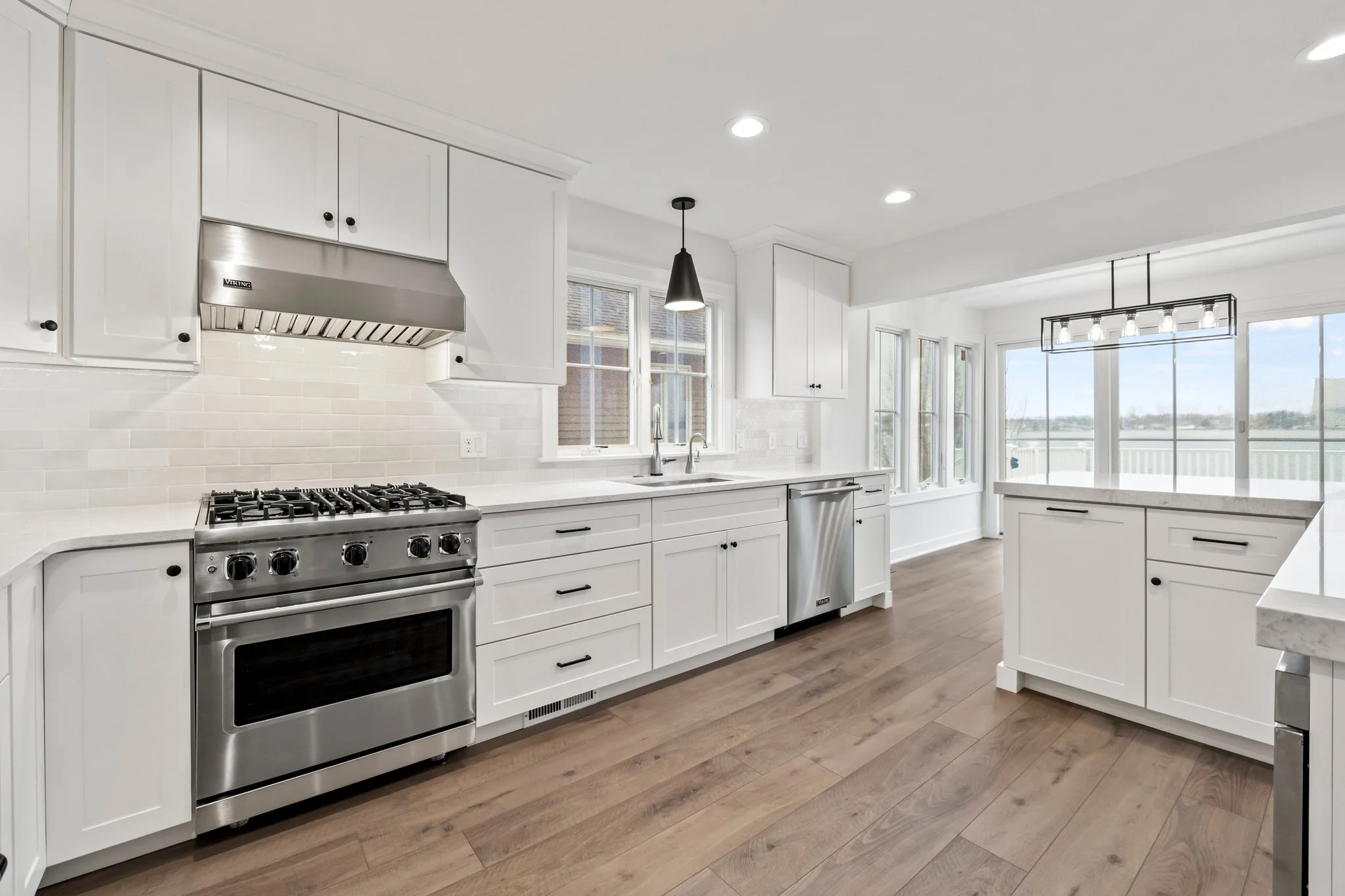 Modern white kitchen with stainless steel appliances and hardwood floors, spacious sunlit dining area with large windows and sliding glass doors.