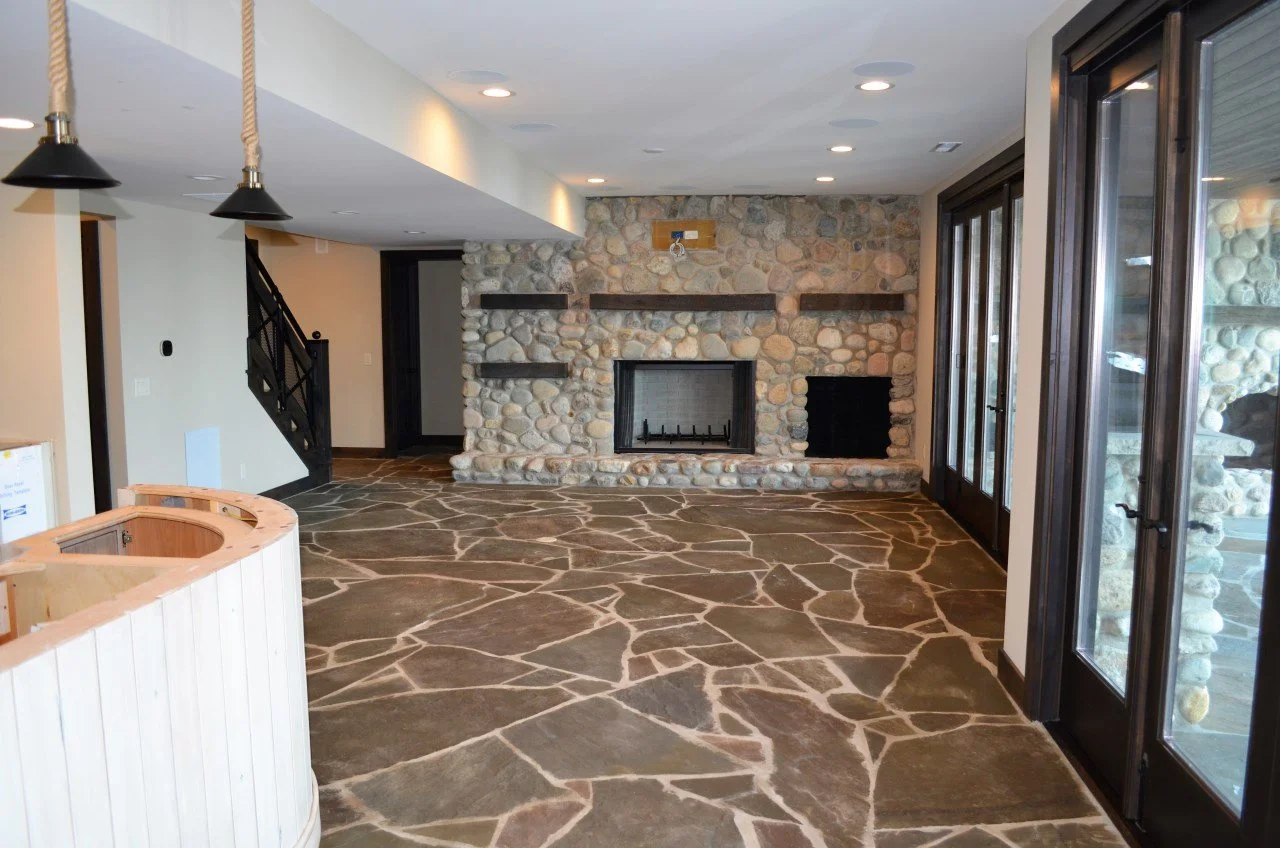 Living room with stone fireplace, stone-tile floor, and French doors leading outside.