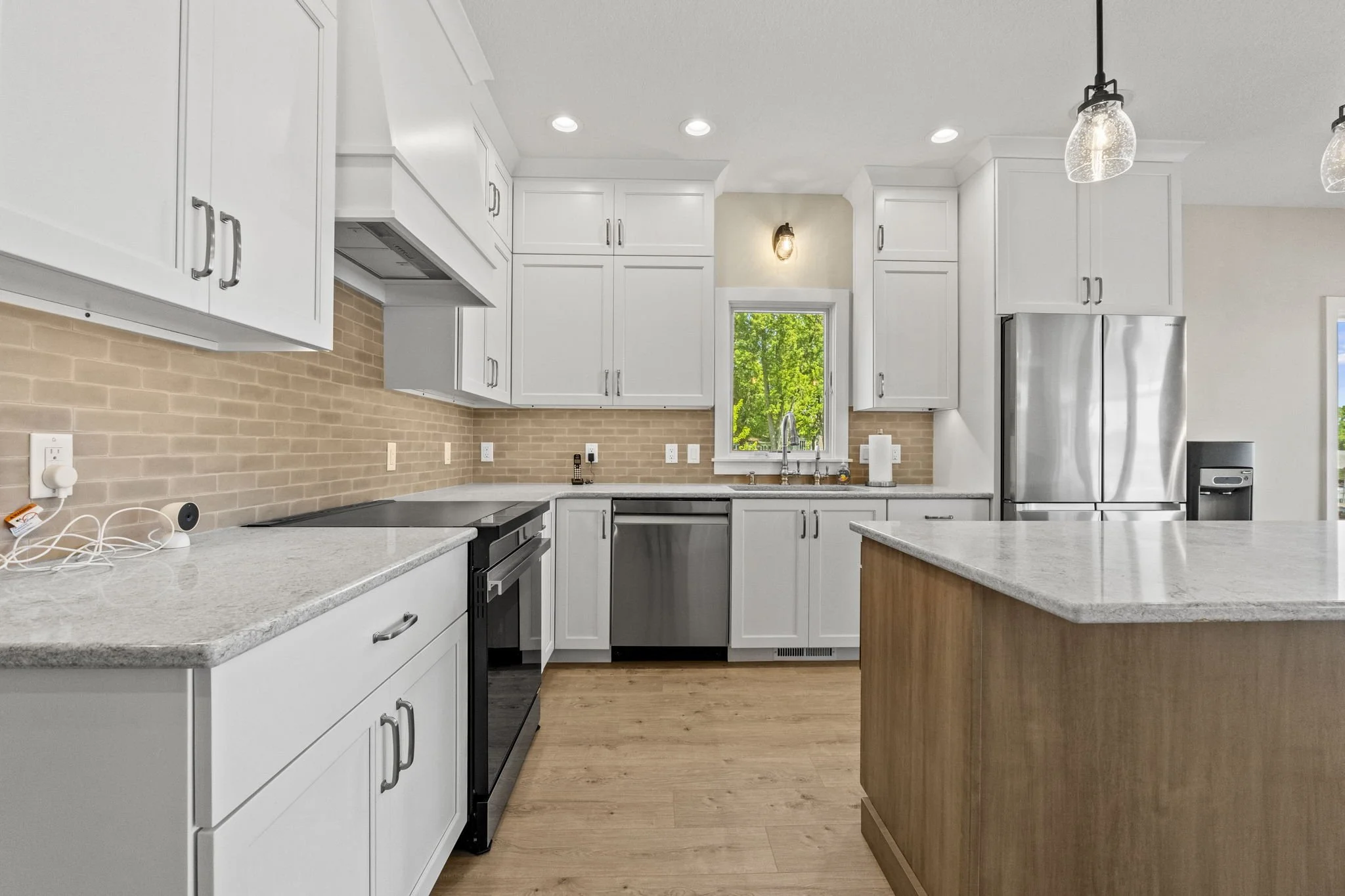 Kitchen with white cabinets, a beige brick backsplash, stainless steel appliances including a refrigerator and dishwasher, and a light wood floor.