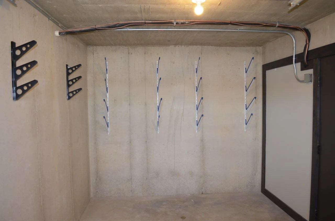 Empty garage with wall-mounted racks and hooks, exposed electrical conduit, and a closed door with a white panel.