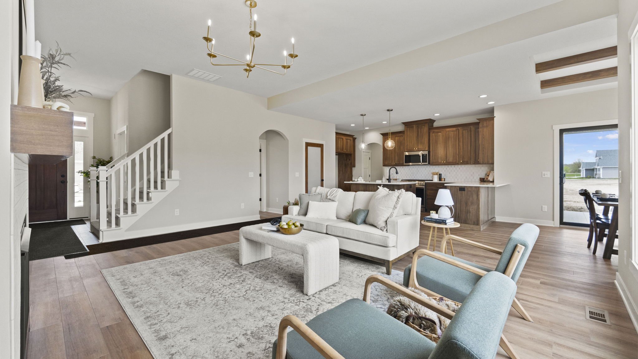 Open-concept living room and kitchen with white sofa, light blue chairs, and wooden cabinetry, natural light, hardwood flooring, and modern decor.