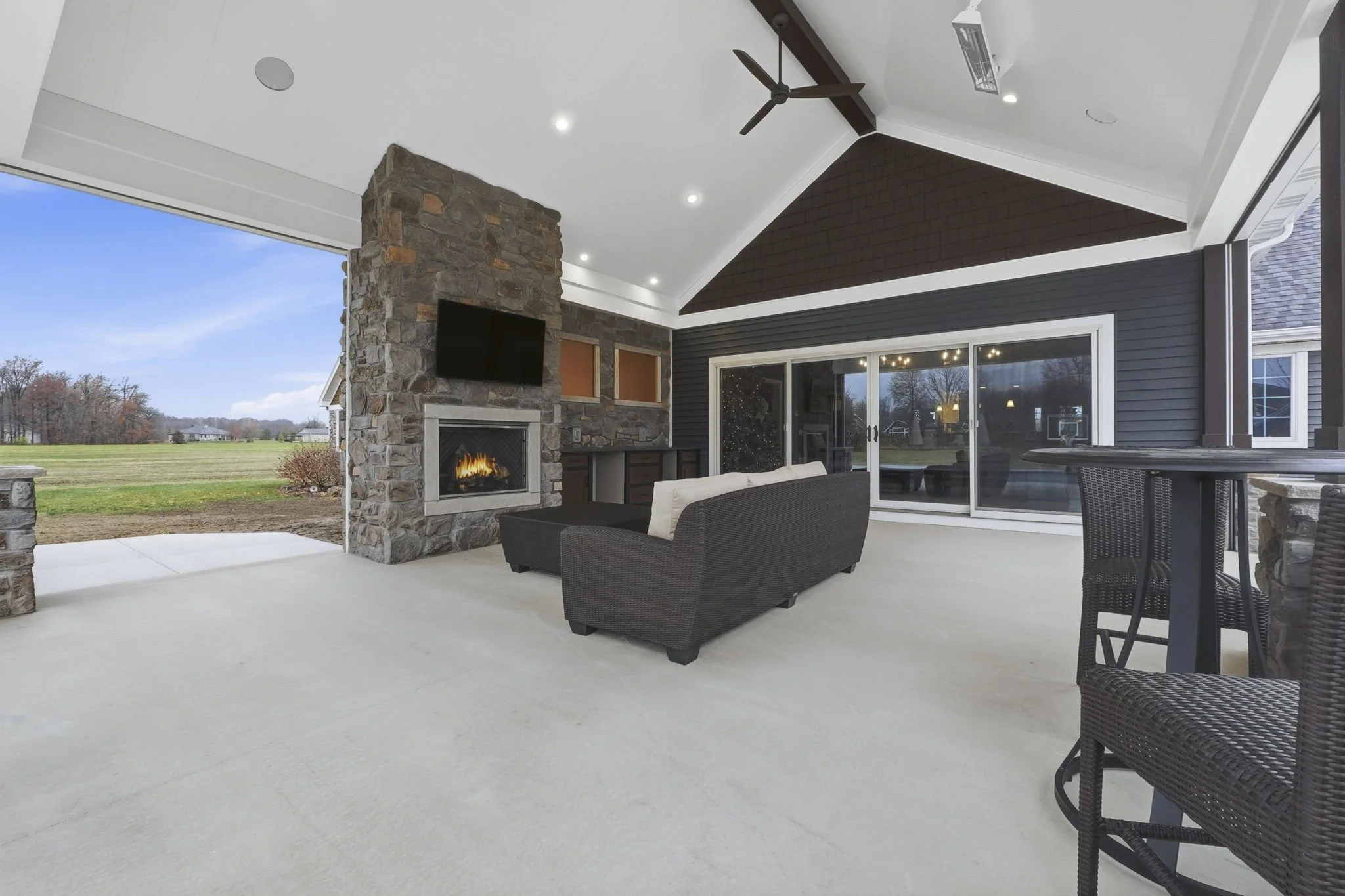 Outdoor patio area with stone fireplace, television, seating, and large sliding glass doors leading to yard.