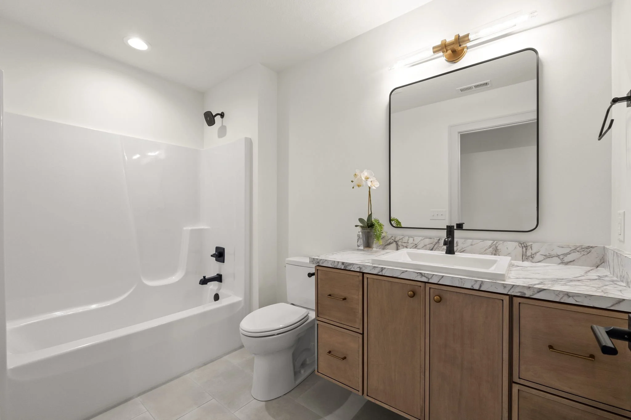 Modern bathroom with white bathtub and shower, toilet, wooden vanity with marble countertop, large mirror, and minimal decor.