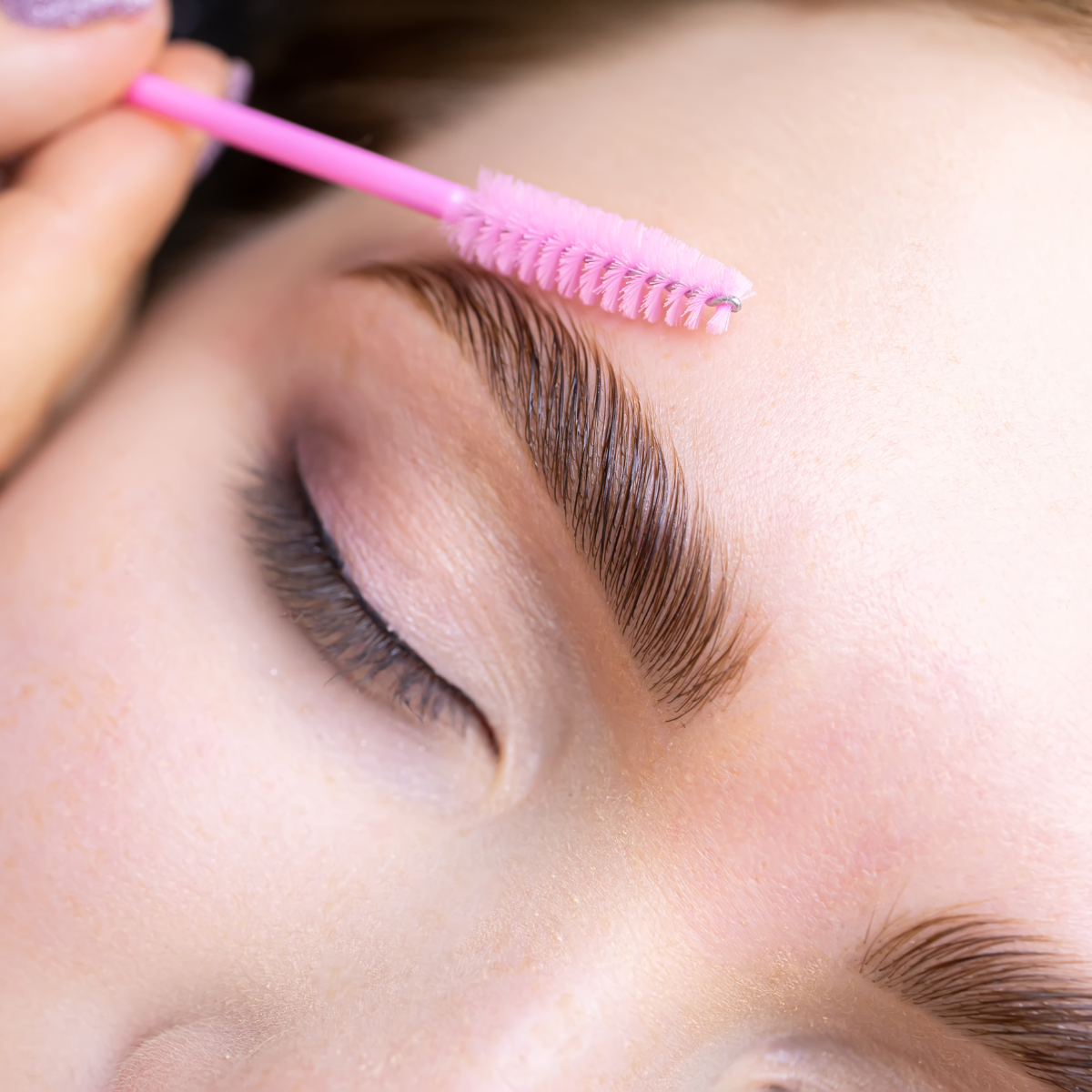 Procedimiento de limpieza o cuidado de las cejas con una cerdas rosa sobre una ceja delgada y bien definida.