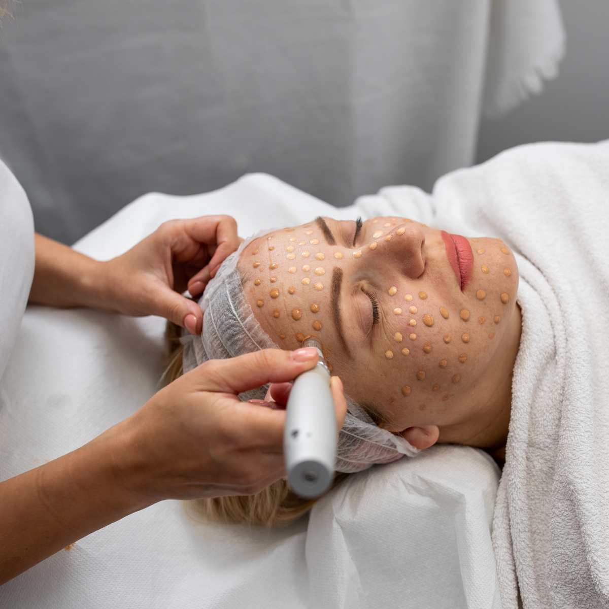 Mujer recibiendo tratamiento facial en spa, con pequeños parches en su rostro y una máquina en mano