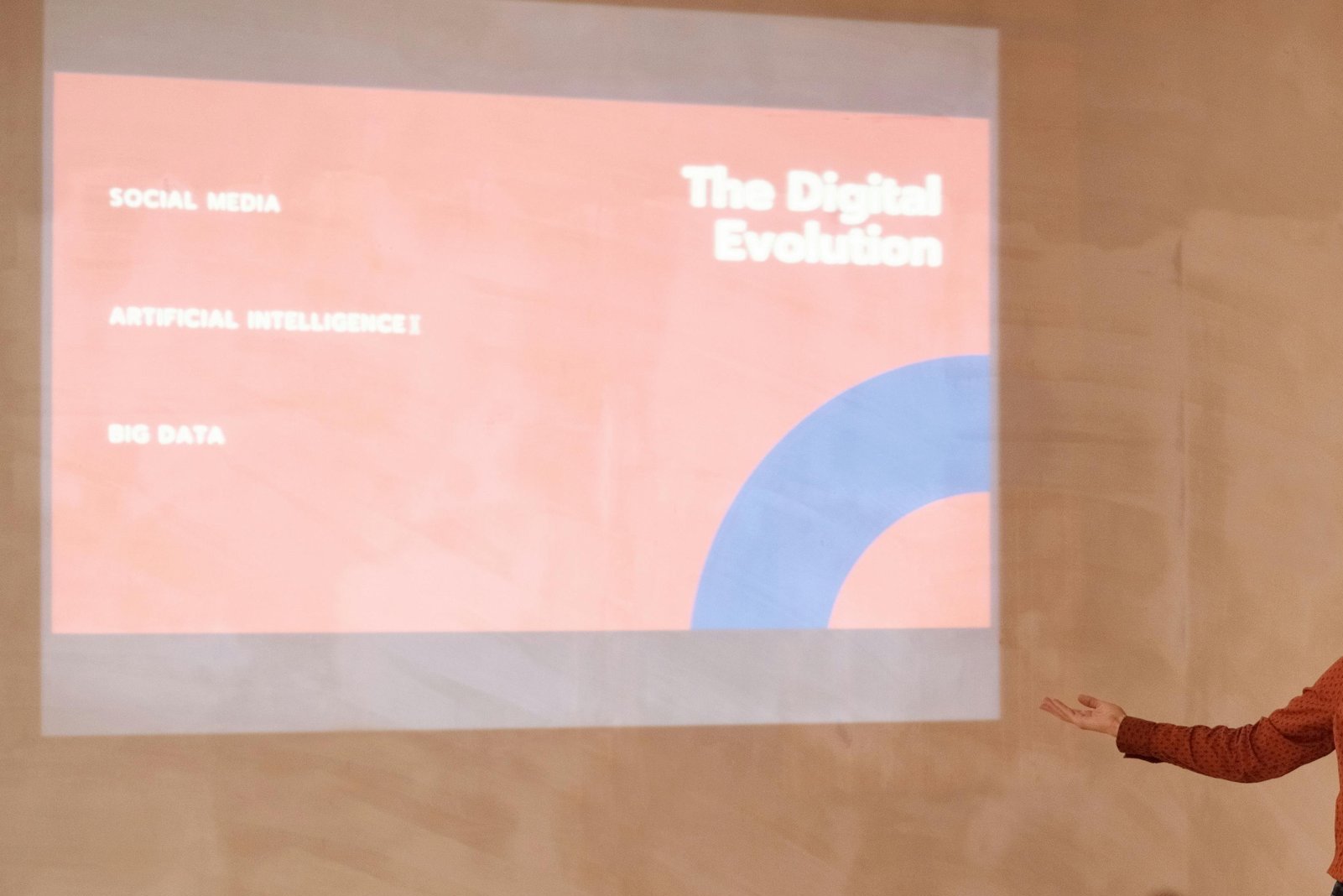 A presentation slide titled 'The Digital Evolution' discussing social media, artificial intelligence, and big data, with an outstretched hand of a person in a brown polka dot shirt pointing towards the slide.