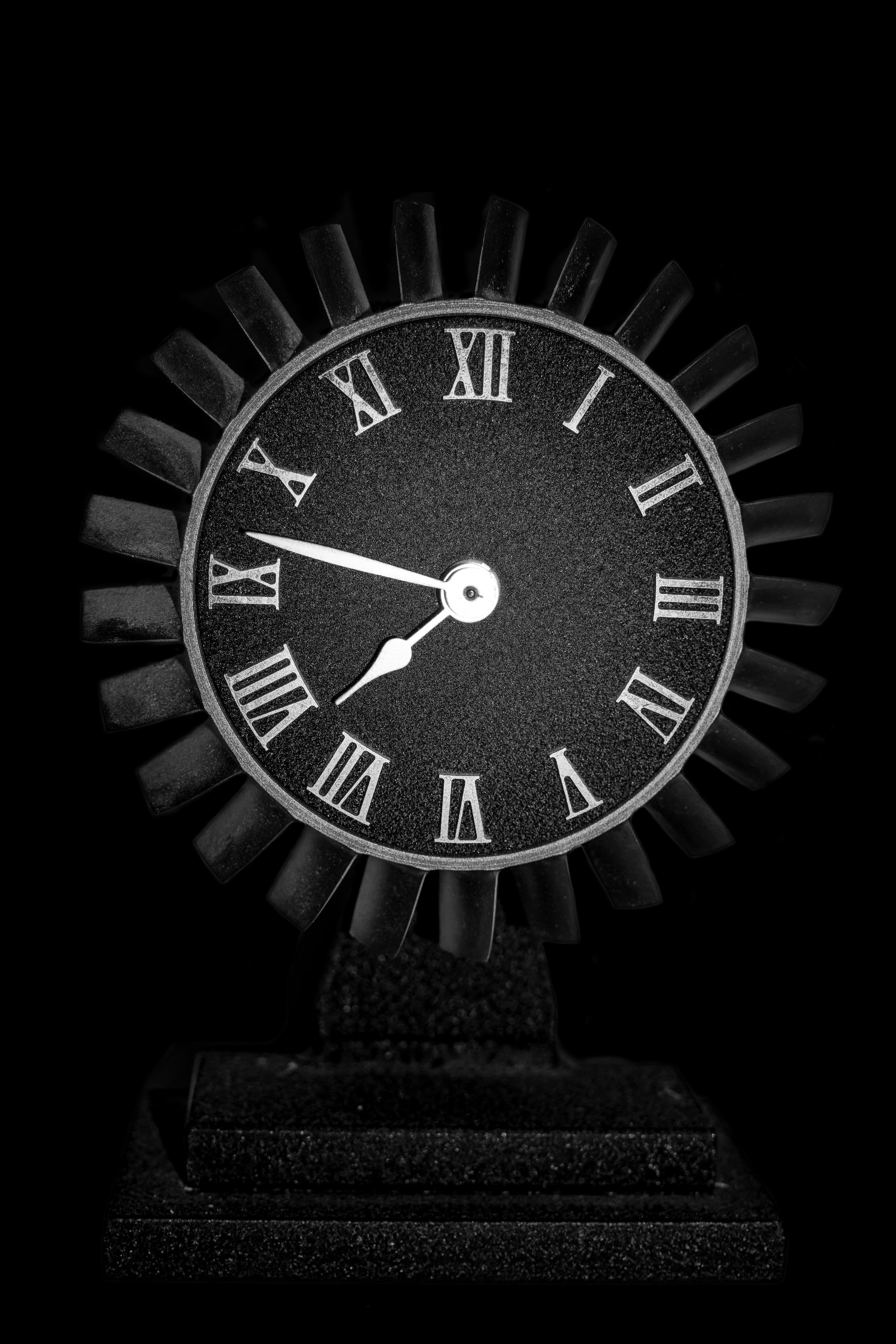 Black analog clock with Roman numerals, showing the time as 6:47, against a dark background.
