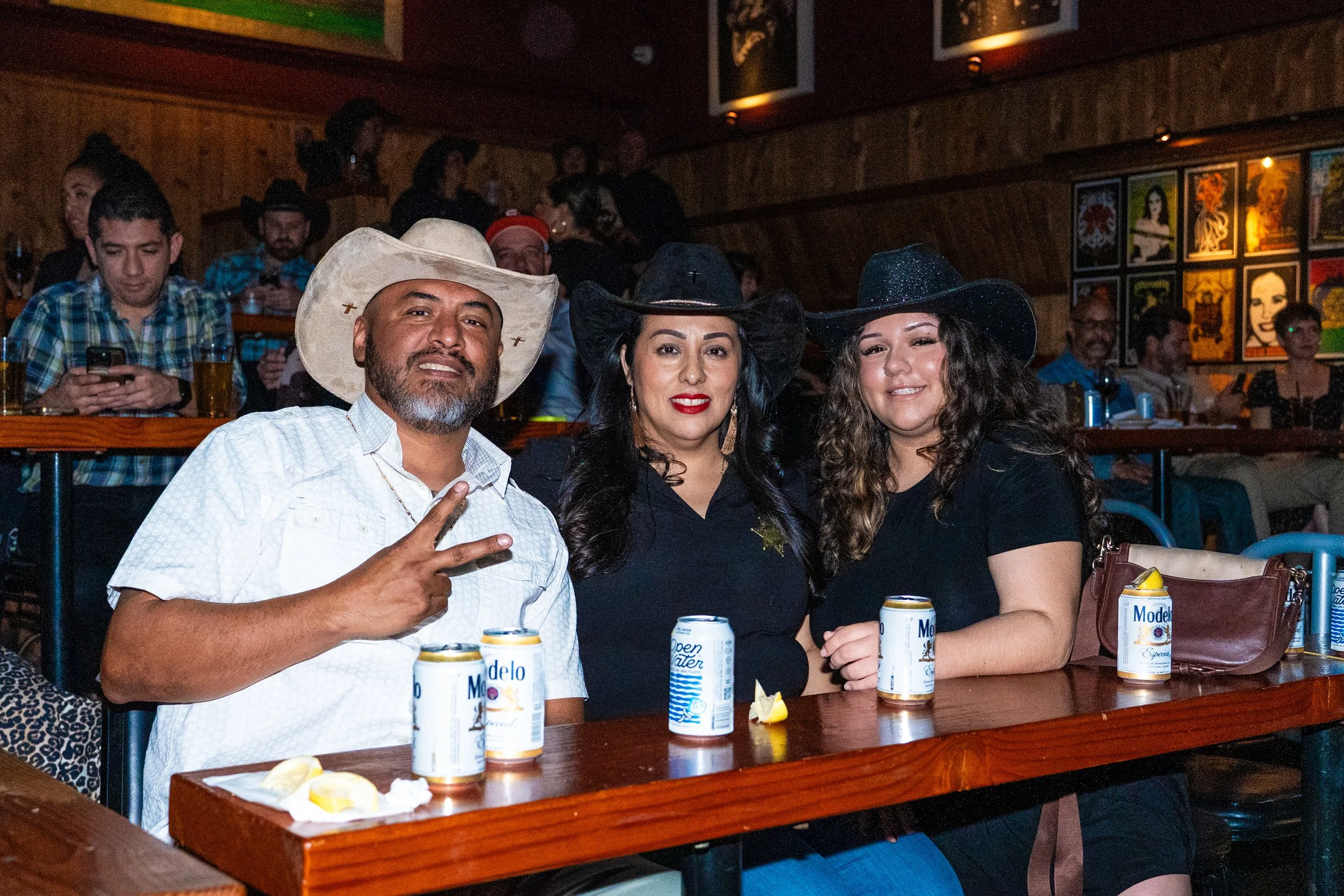Three people sitting at a bar or restaurant, wearing cowboy hats, with drinks and lemon wedges on the table, smiling.