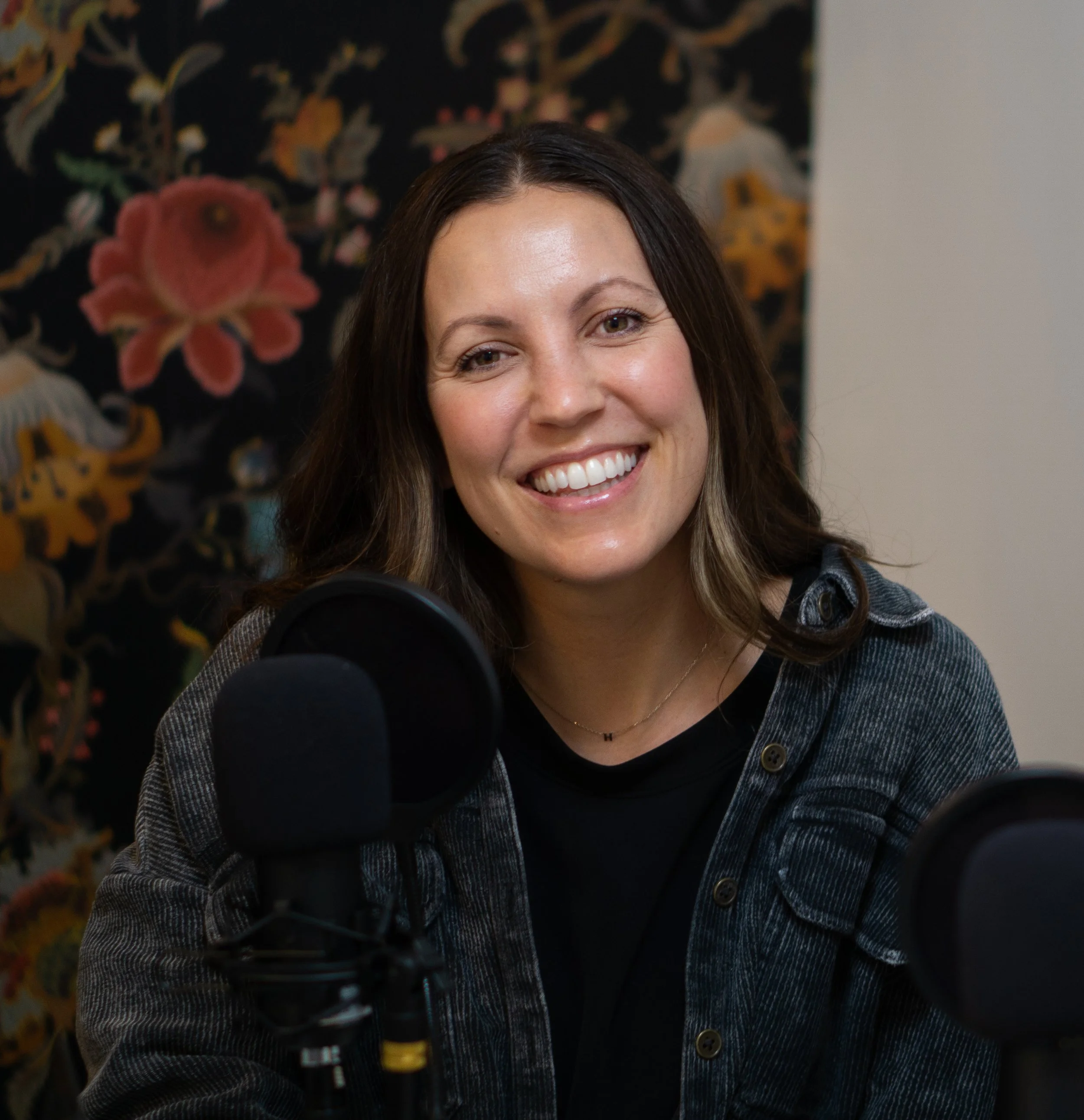 Woman with brown hair smiling at a microphone in a recording studio.