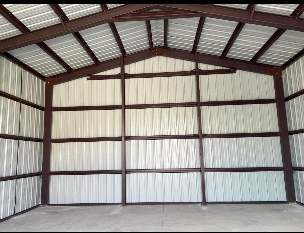 Interior view of an empty metal storage shed with light-colored corrugated metal walls and a metal roof with brown framing.