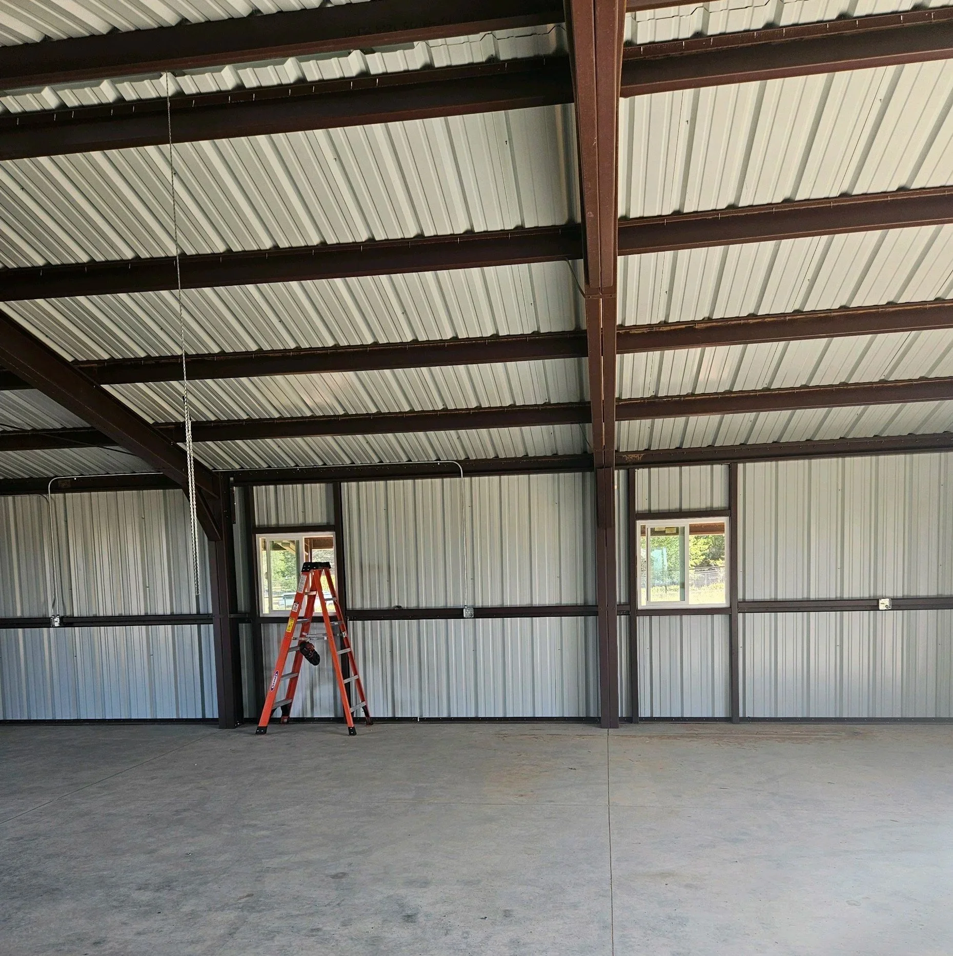 Empty metallic garage or warehouse space with a concrete floor, metal walls, and ceiling, and a red ladder leaning against the wall.