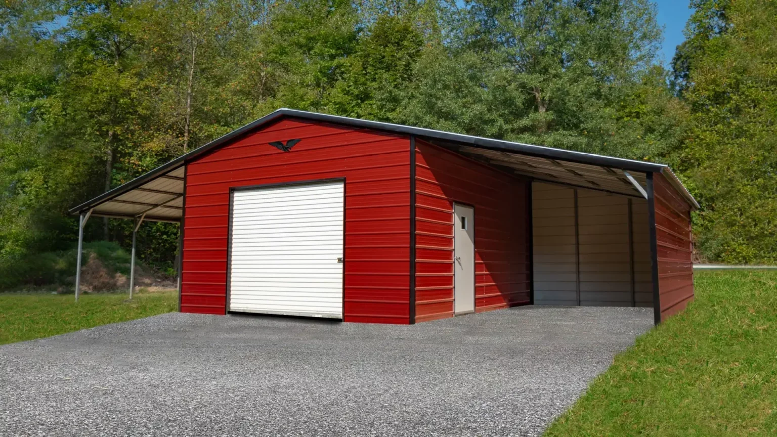 Red metal storage building with a white roll-up door, a smaller side door, and a covered parking area, surrounded by green trees and grass