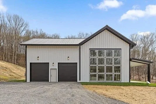 Modern garage with two black doors and a large glass window on the right, surrounded by a grassy yard and leafless trees in the background.
