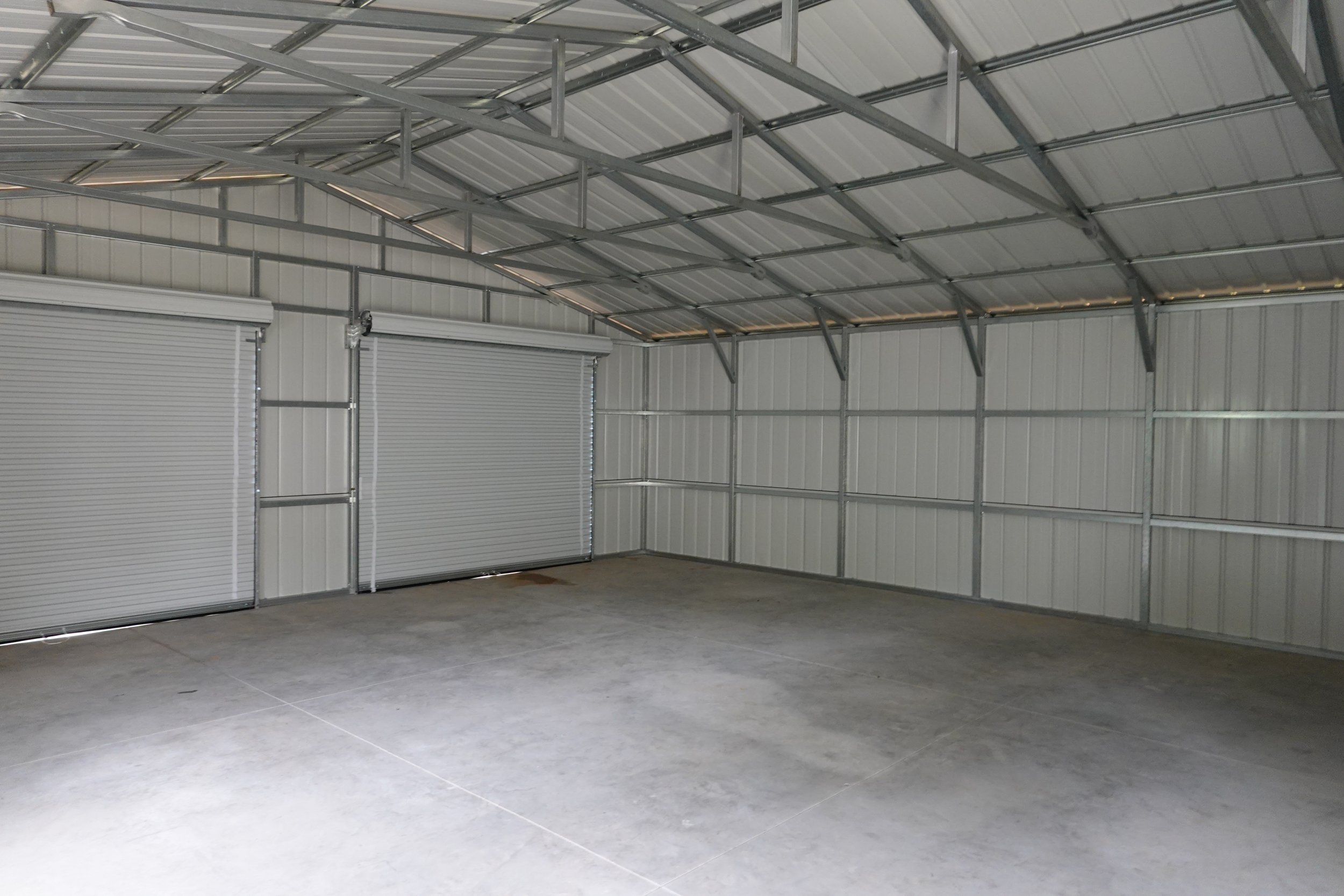 Empty metal garage with concrete floor and two closed roll-up doors.