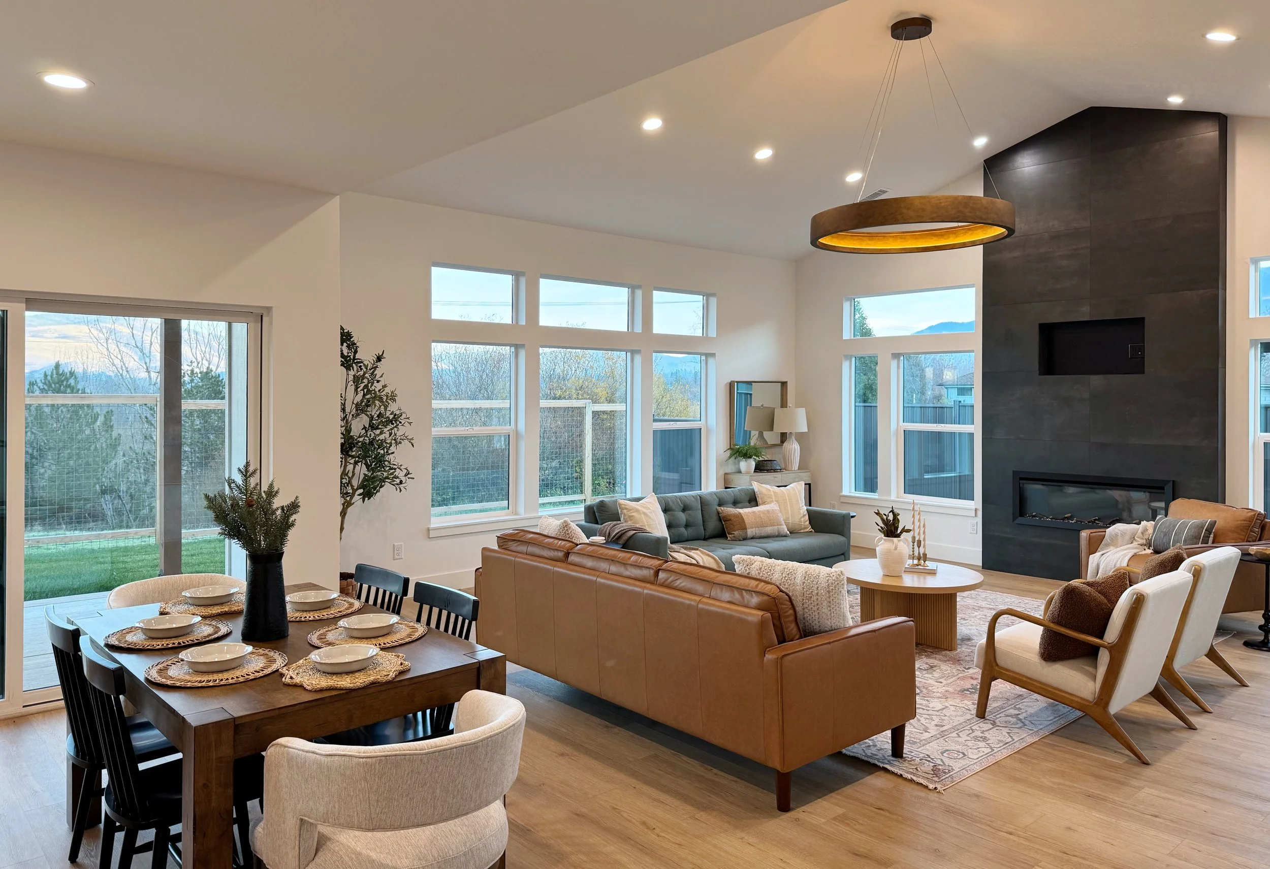 Open-concept living room and dining area with modern furniture, large windows, a fireplace, and a view of the outdoors.