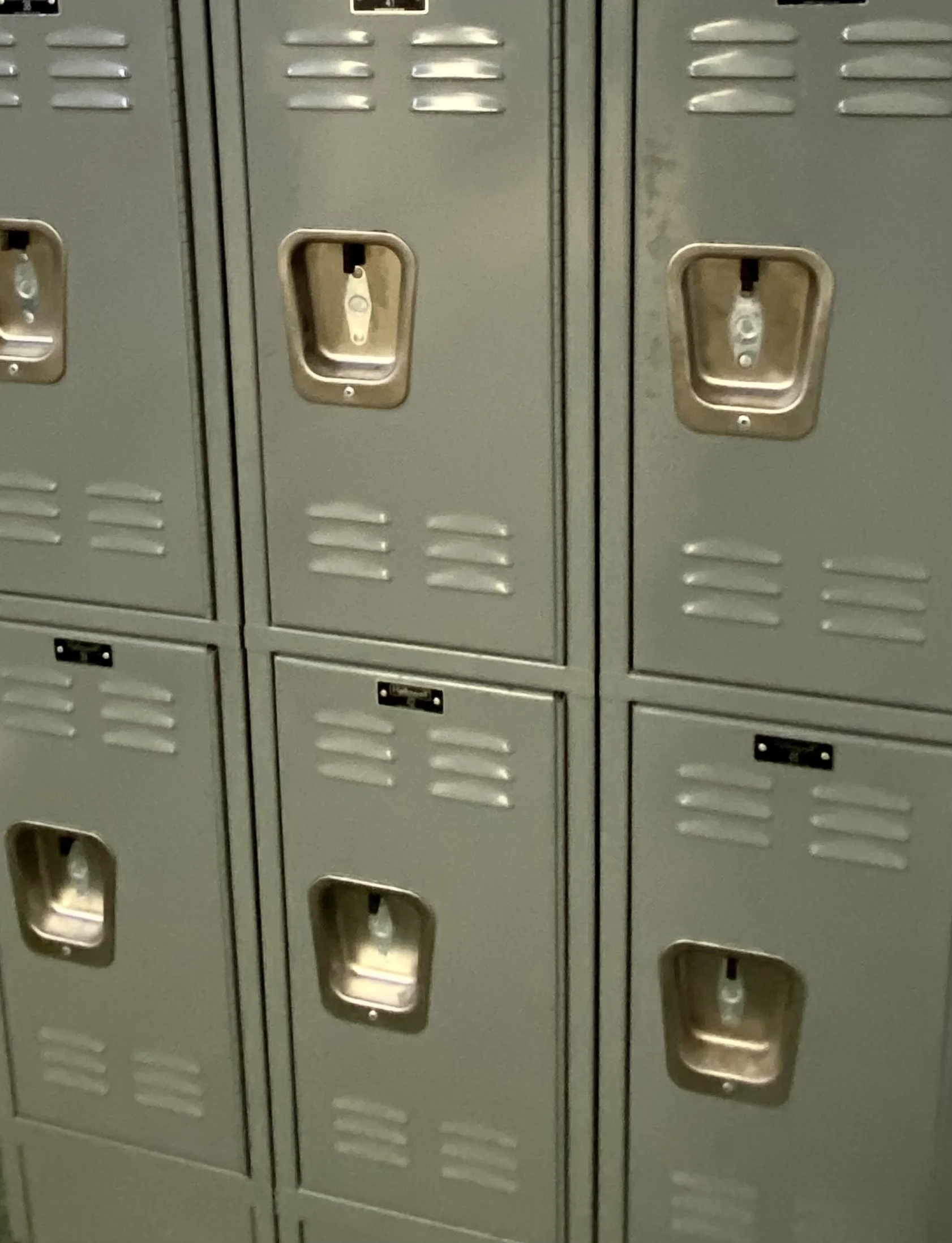 A row of gray gym lockers with ventilated doors, some of which have silver combination locks.