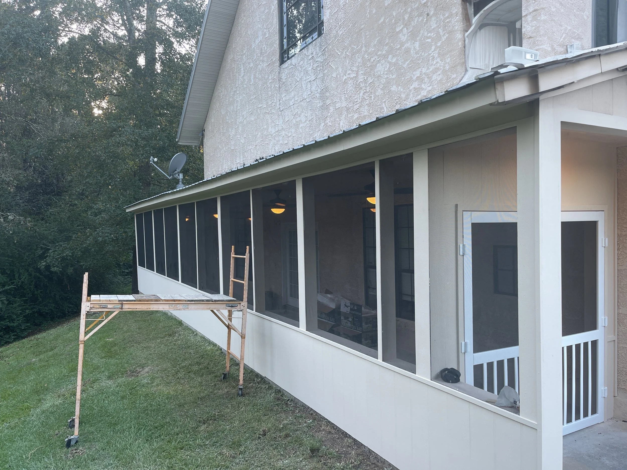 A house with a screened-in porch under construction, with a wooden scaffold and a ladder outside.
