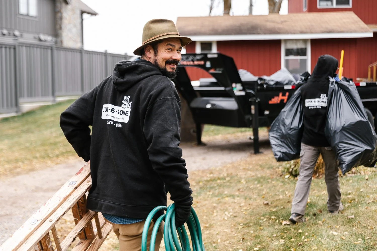 Junk Expert hauling garage items to a dump trailer and another man hauling garbage bags