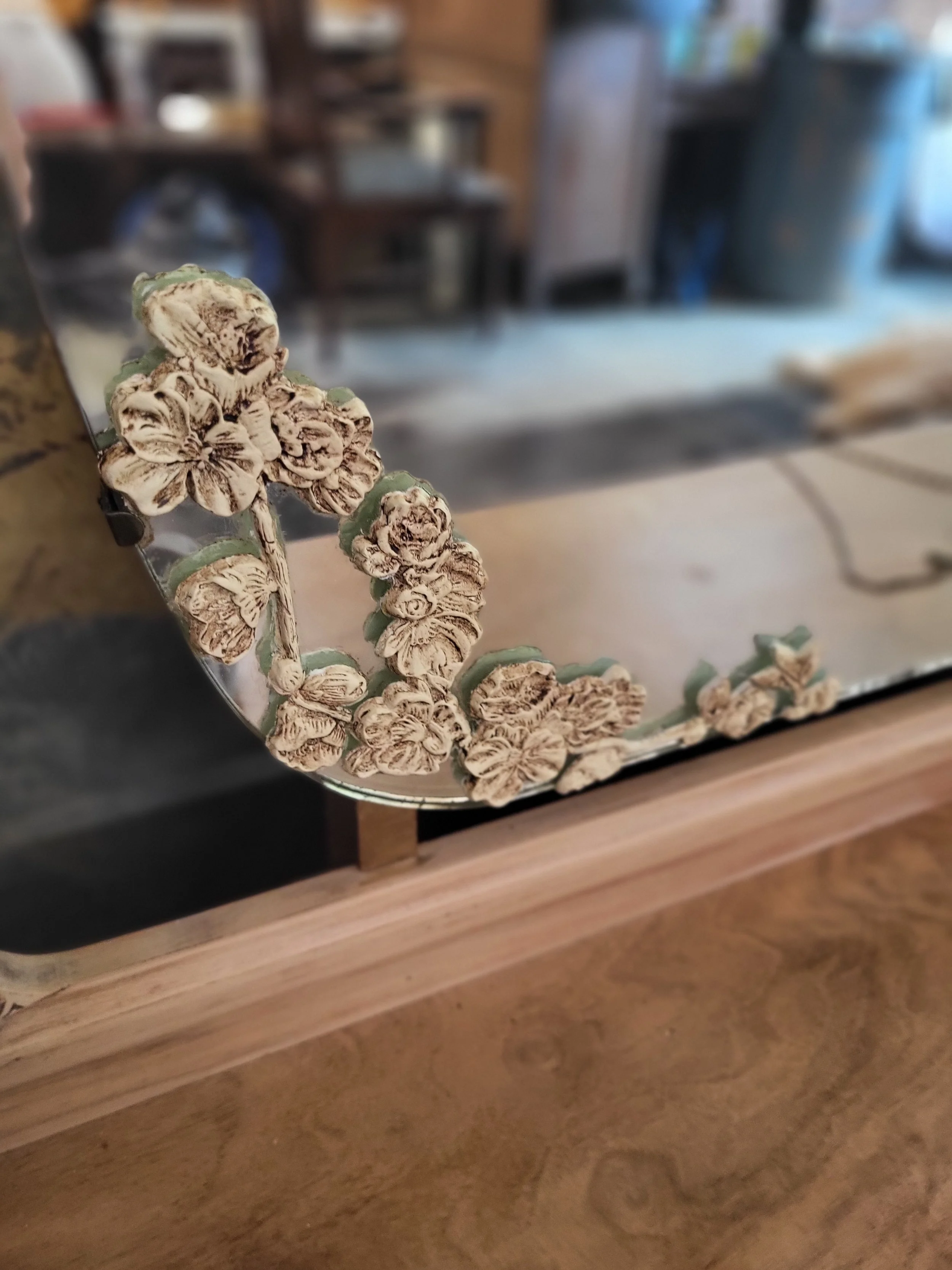 Decorative mirror with a floral design on its corner, placed on a wooden surface in a kitchen setting.