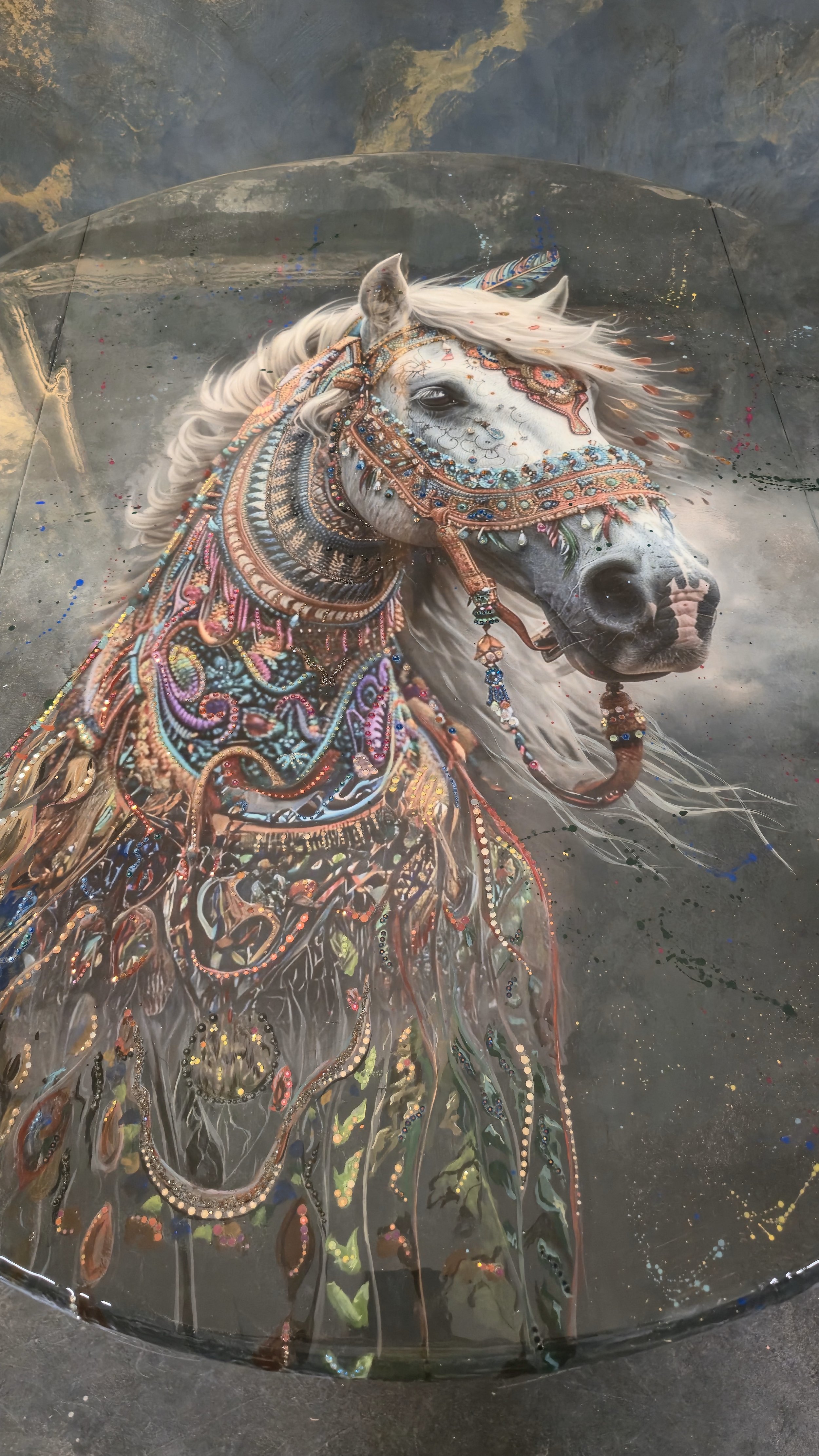A white horse with elaborate, colorful, beaded and embroidered jewelry and decorations, lying inside a transparent enclosure.
