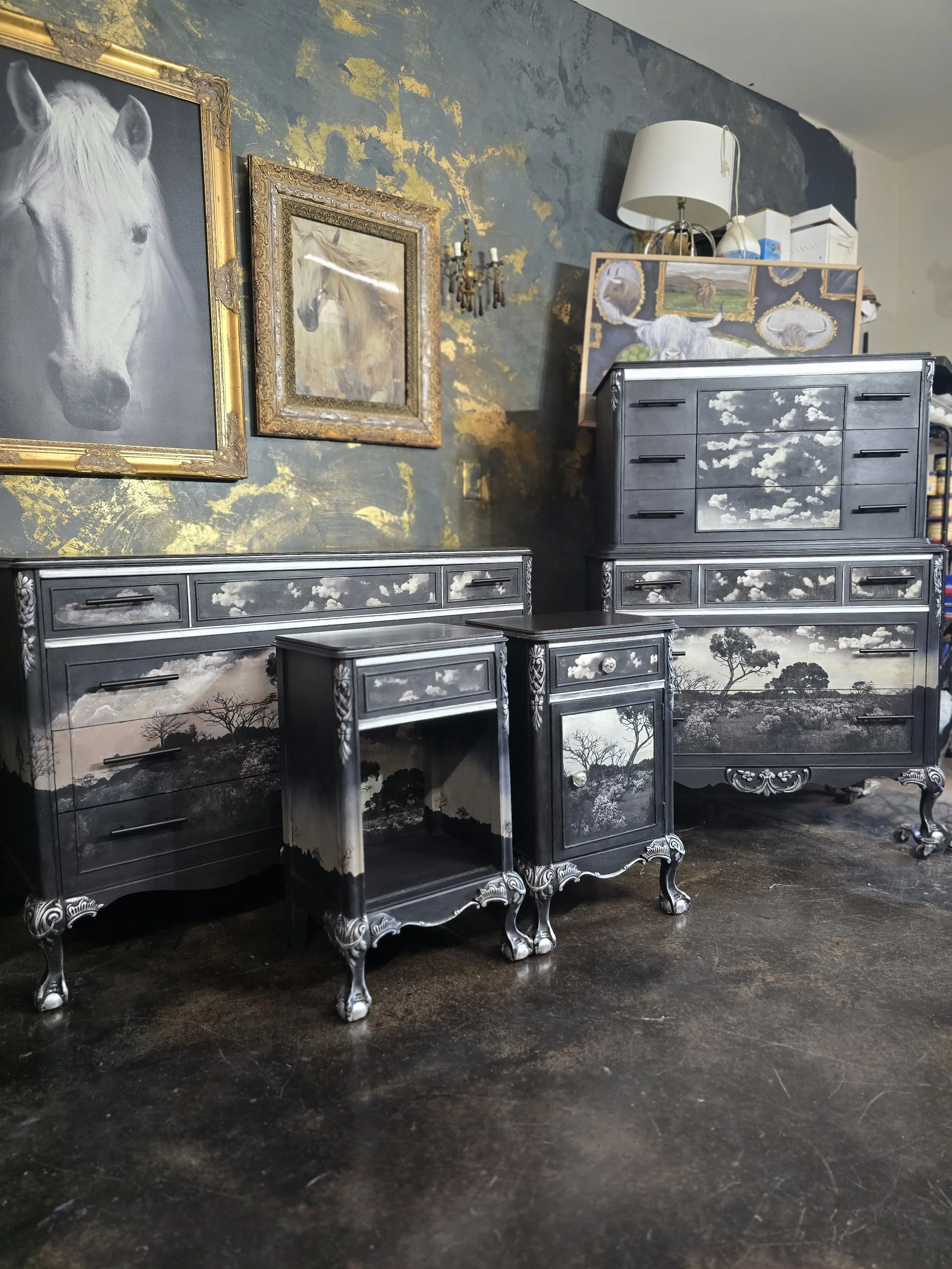black furniture with landscape and sky paintings, including trees and clouds, set against a dark wall with gold accents, with framed horse portraits hanging above.