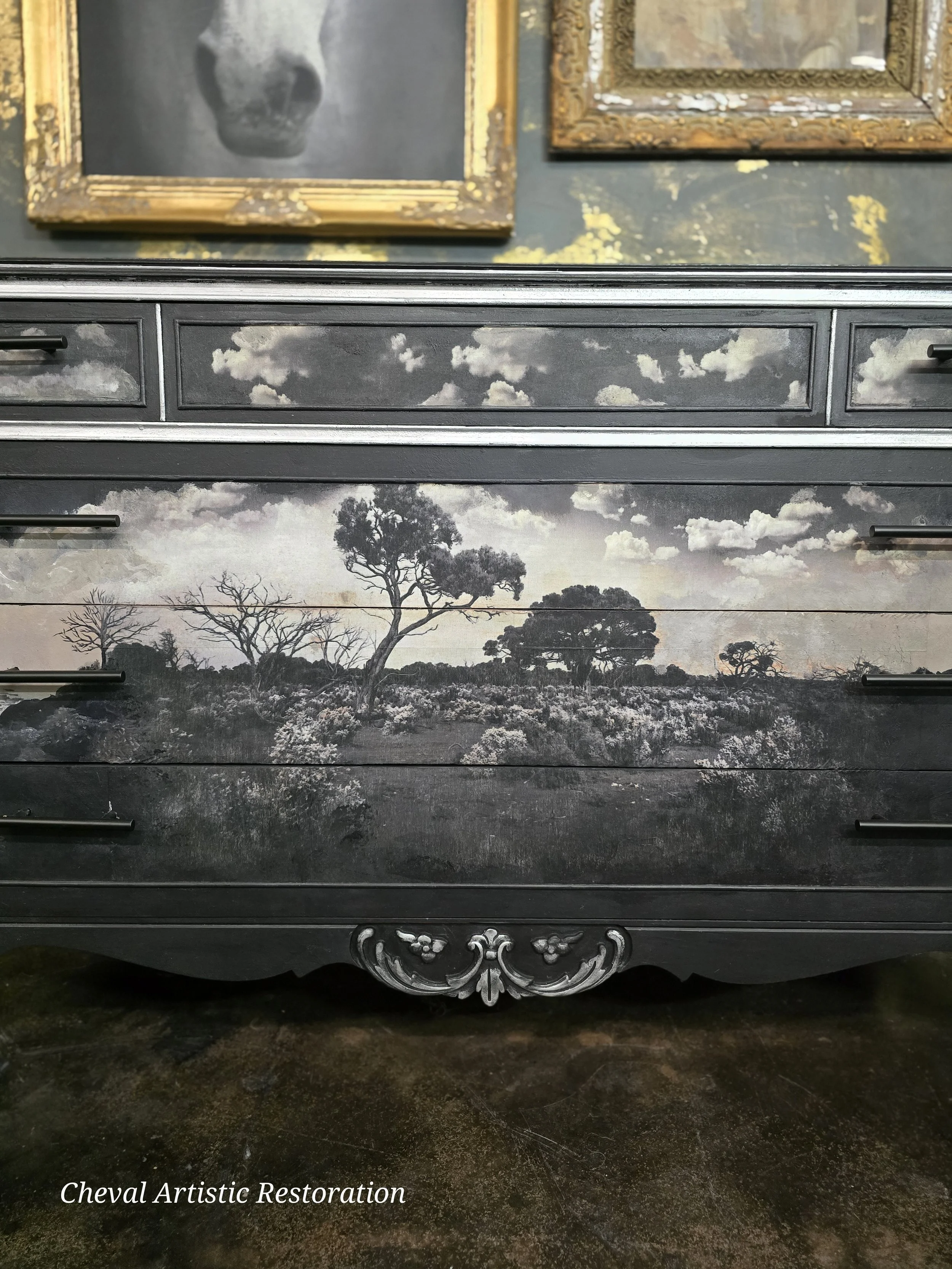 A black dresser with a landscape painting of trees and clouds in black and white, labeled 'Cheval Artistic Restoration'.