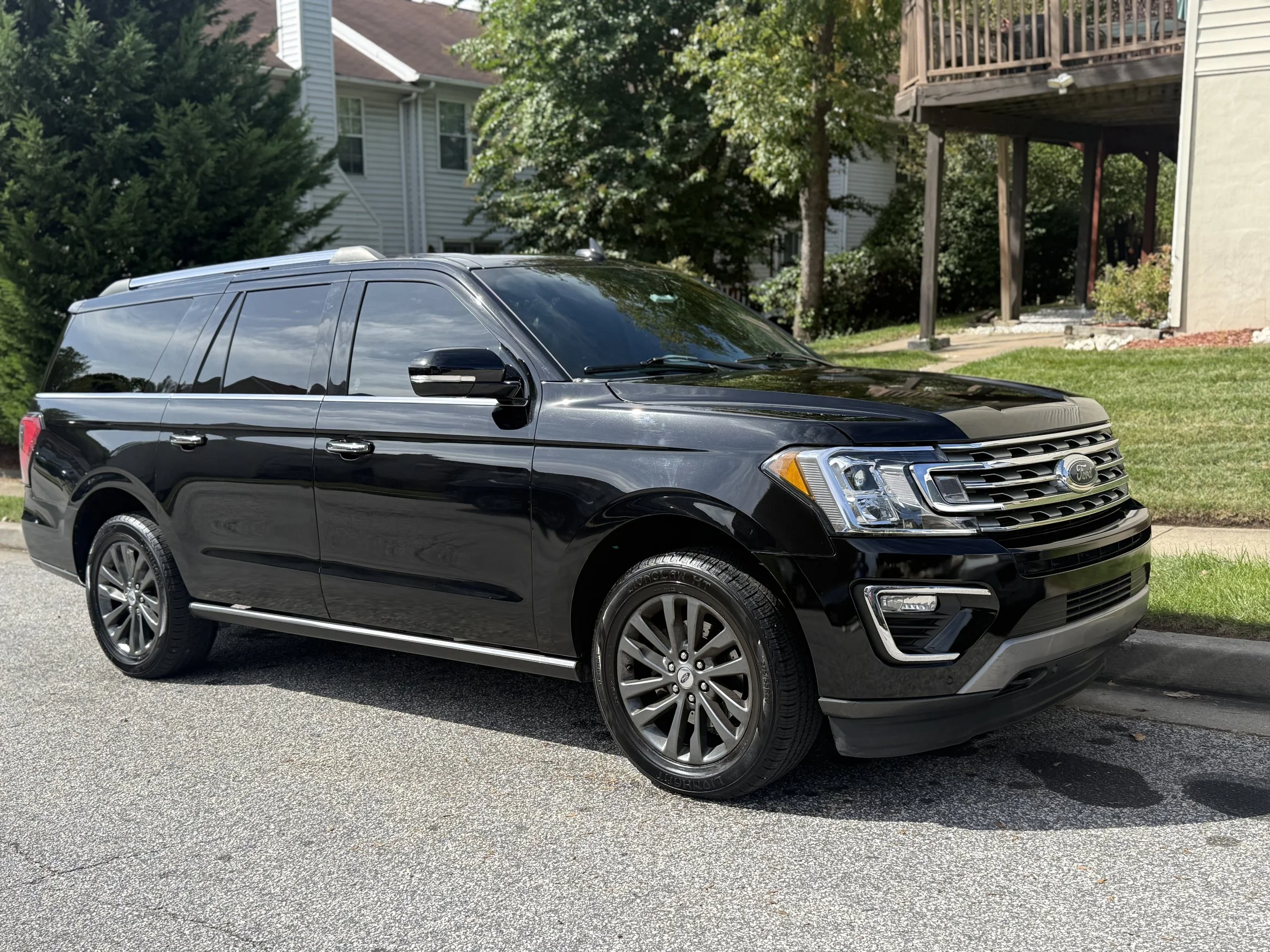 Black Ford SUV parked on street with houses and greenery in the background.