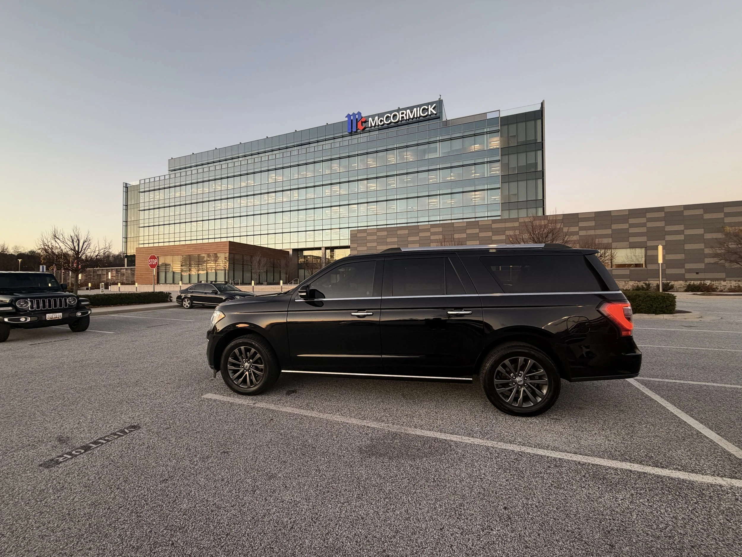 A black SUV parked in a parking lot in front of a modern glass office building with the McCormick sign on top at sunset.