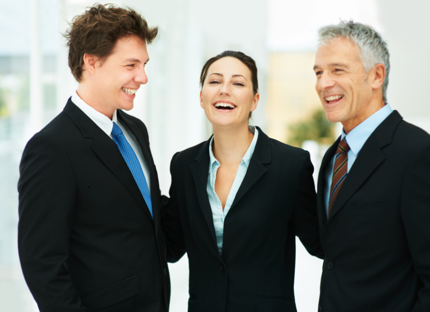 Three businesspeople in formal attire smiling and talking in an office setting.