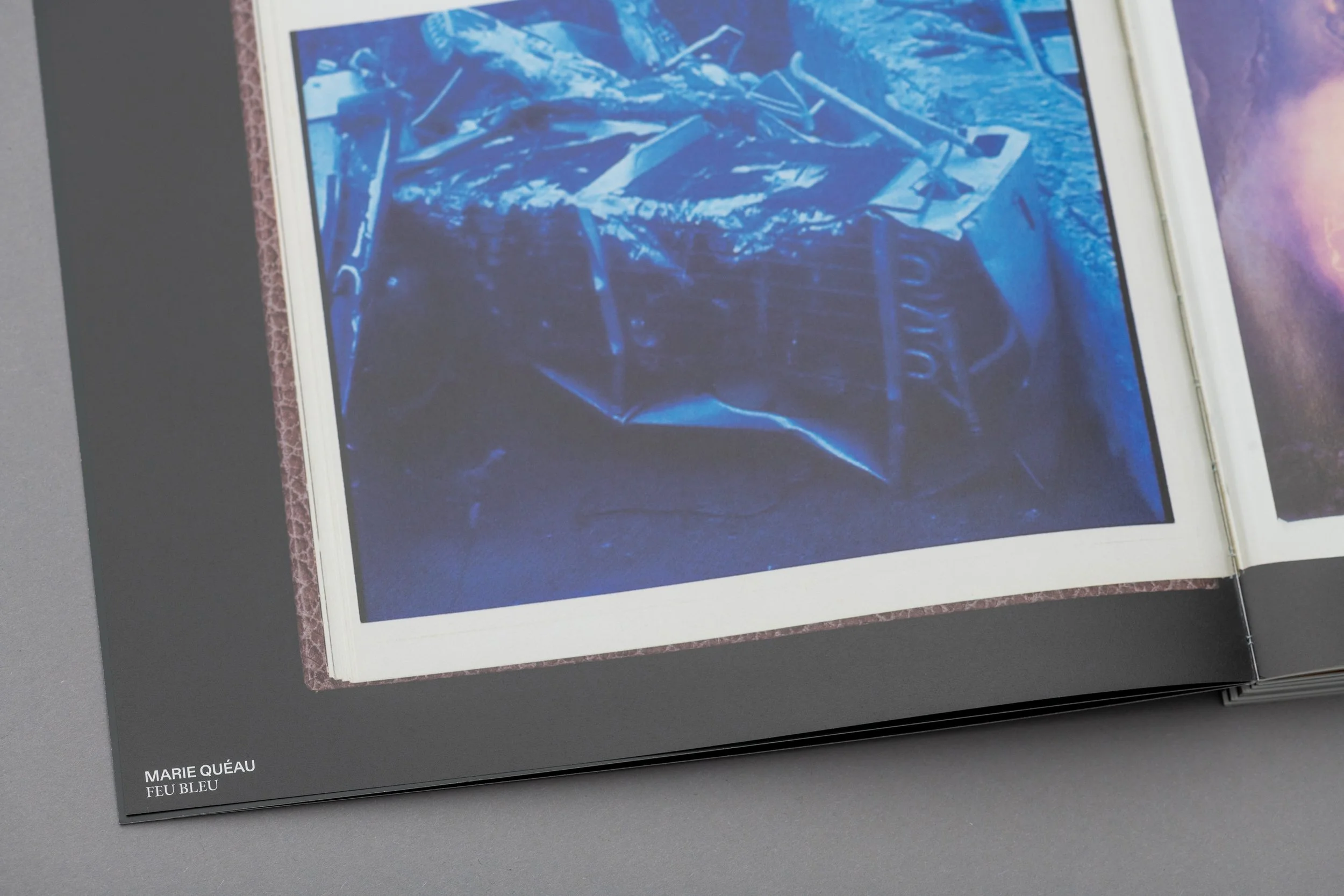 Una foto di un libro aperto che mostra un'immagine blu di un oggetto astratto o una scultura. Nell'angolo inferiore sinistro c'è la scritta "MARIE QUÉAU FEU BLEU".