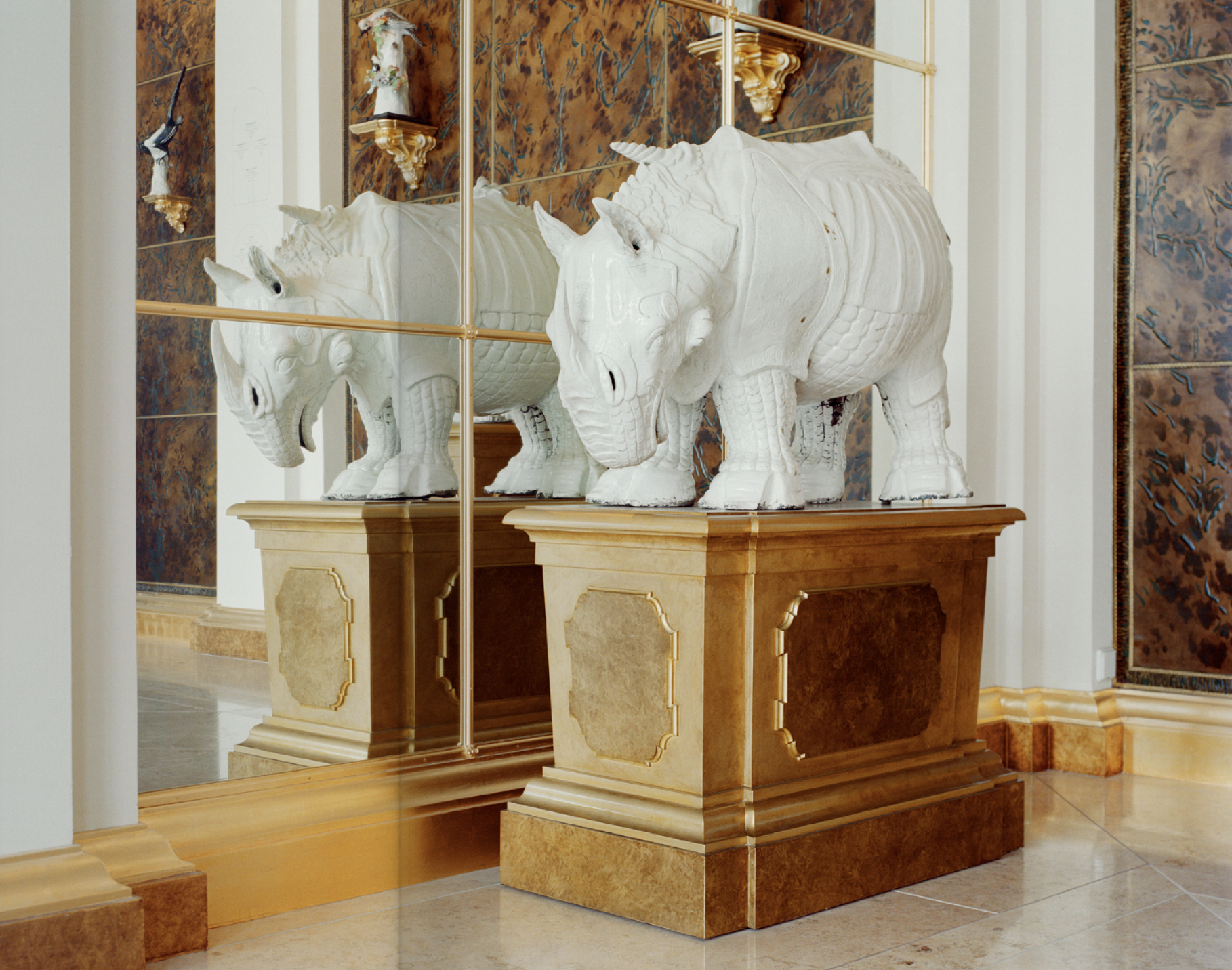 Statua di due ippopotami bianchi in stile classico, poste su un pedestal di marmo, vicino a pareti decorate con pannelli in stile artistico, e una parete di specchi che riflette le statue.