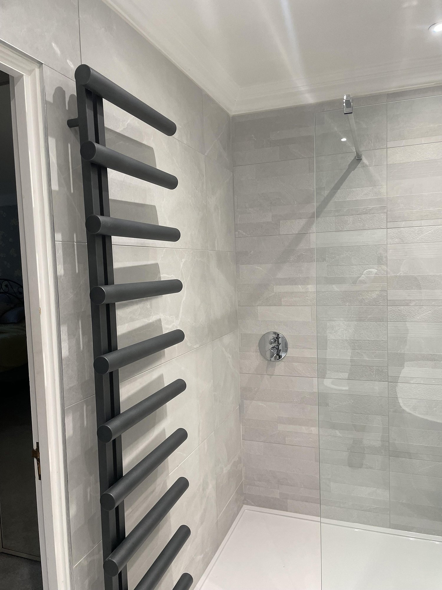 A modern bathroom shower with a grey towel warmer mounted on a light grey tiled wall.