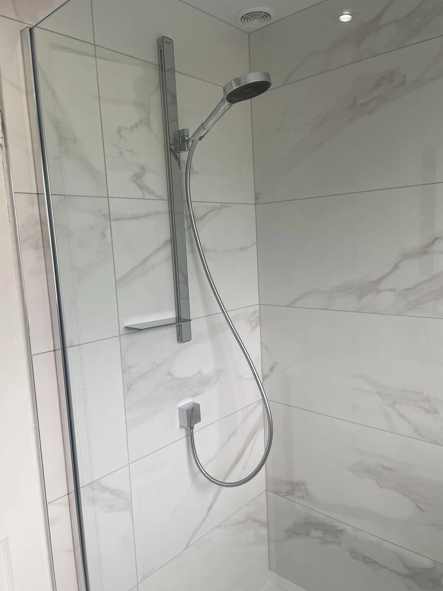 Shower with white marble tiles and a chrome showerhead with an adjustable hose.