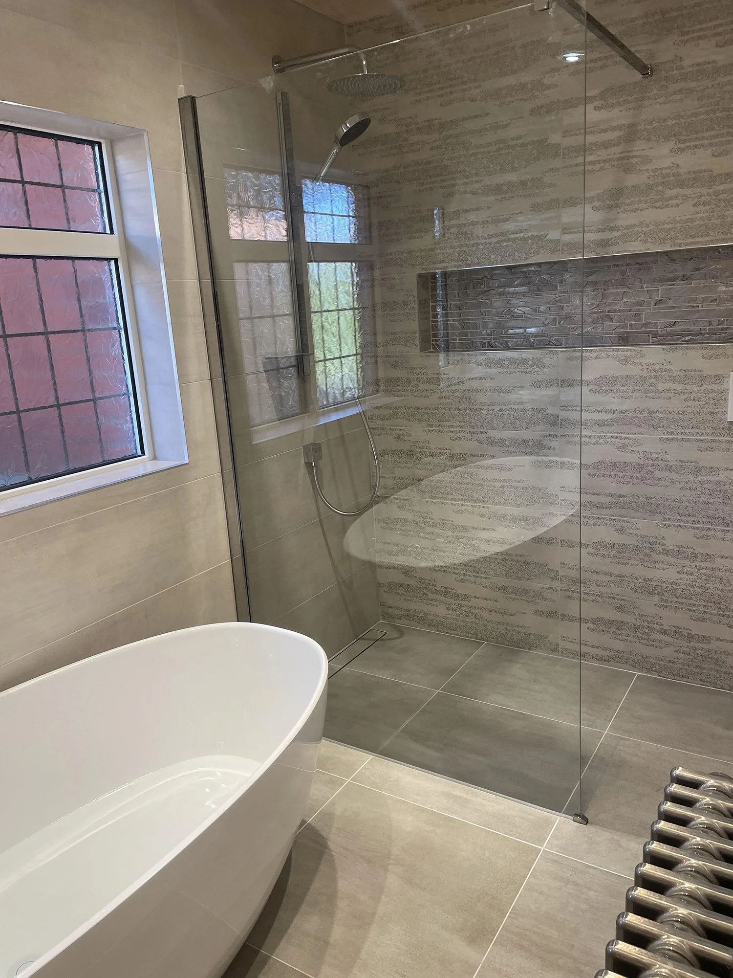 Modern bathroom with a freestanding bathtub, a glass-enclosed shower, a window, and a metal towel radiator.