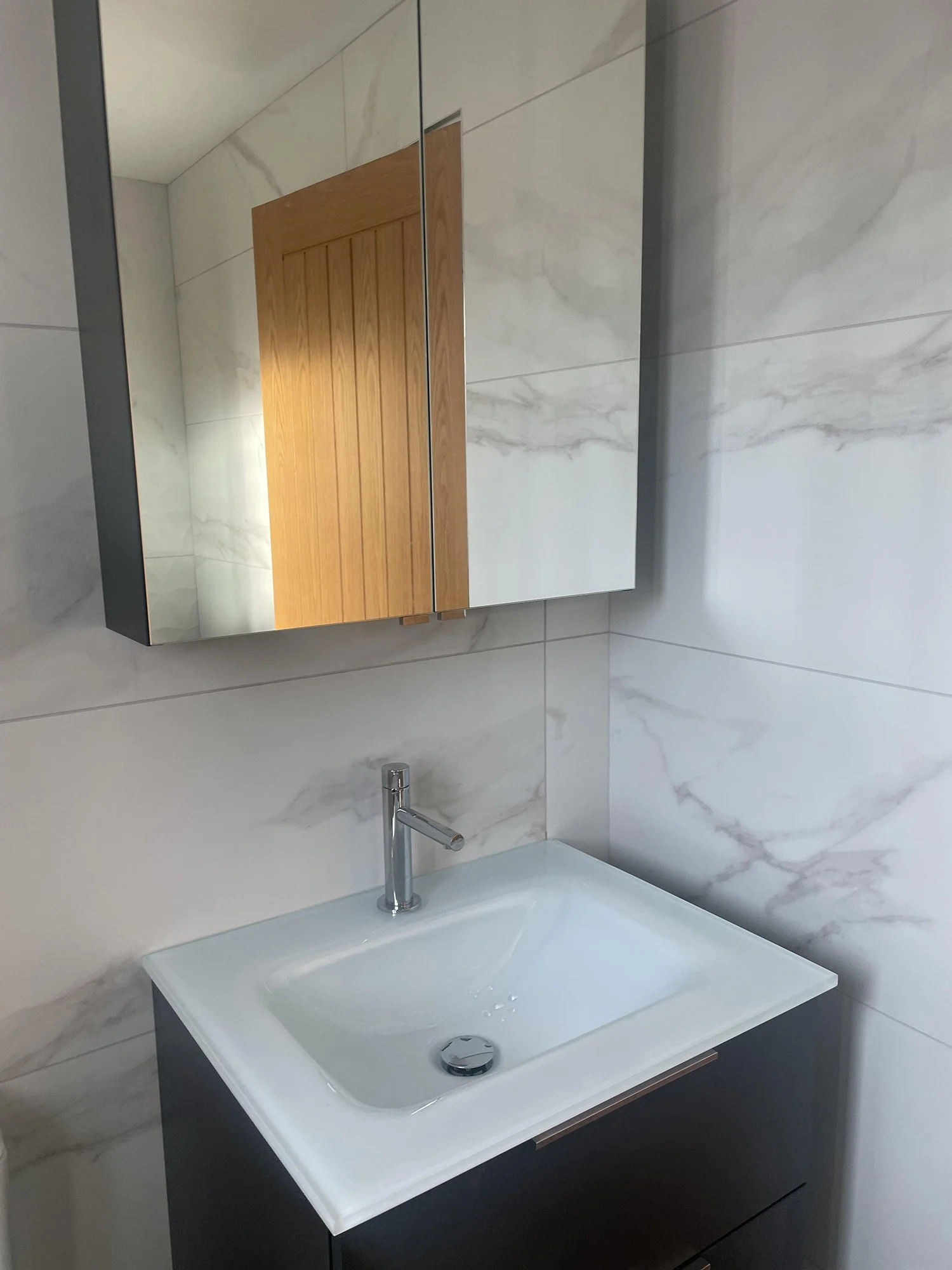 Bathroom sink with mirror cabinet above, marble wall tiles, and a modern faucet.