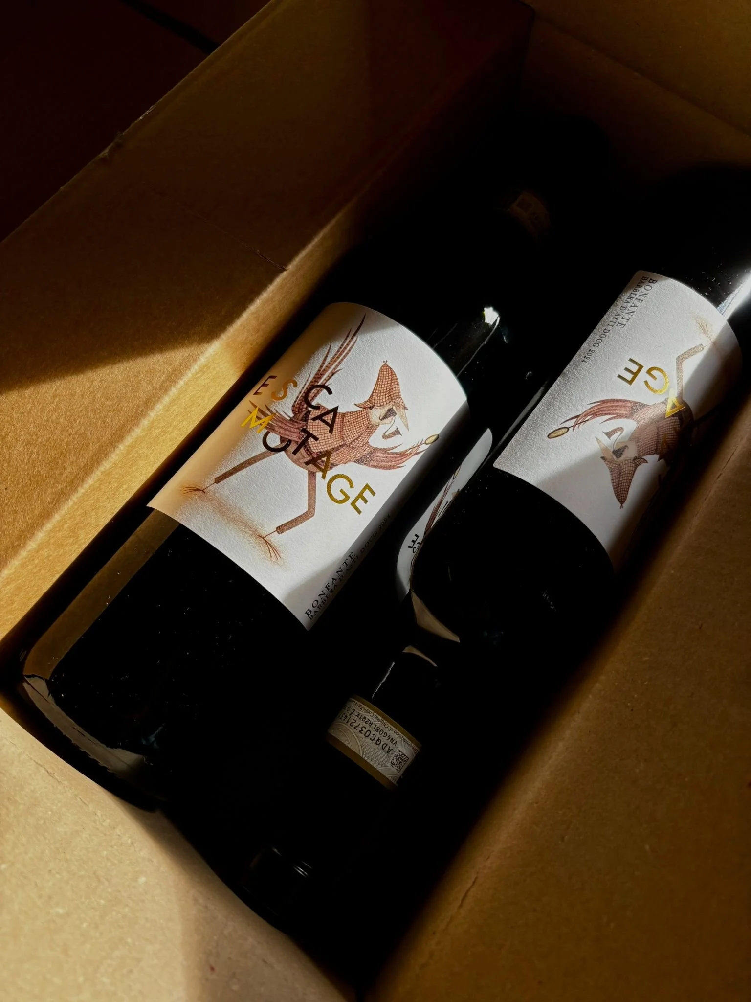 Due bottiglie di vino con etichette che raffigurano un uccello stilizzato e una scatola di cartone.
