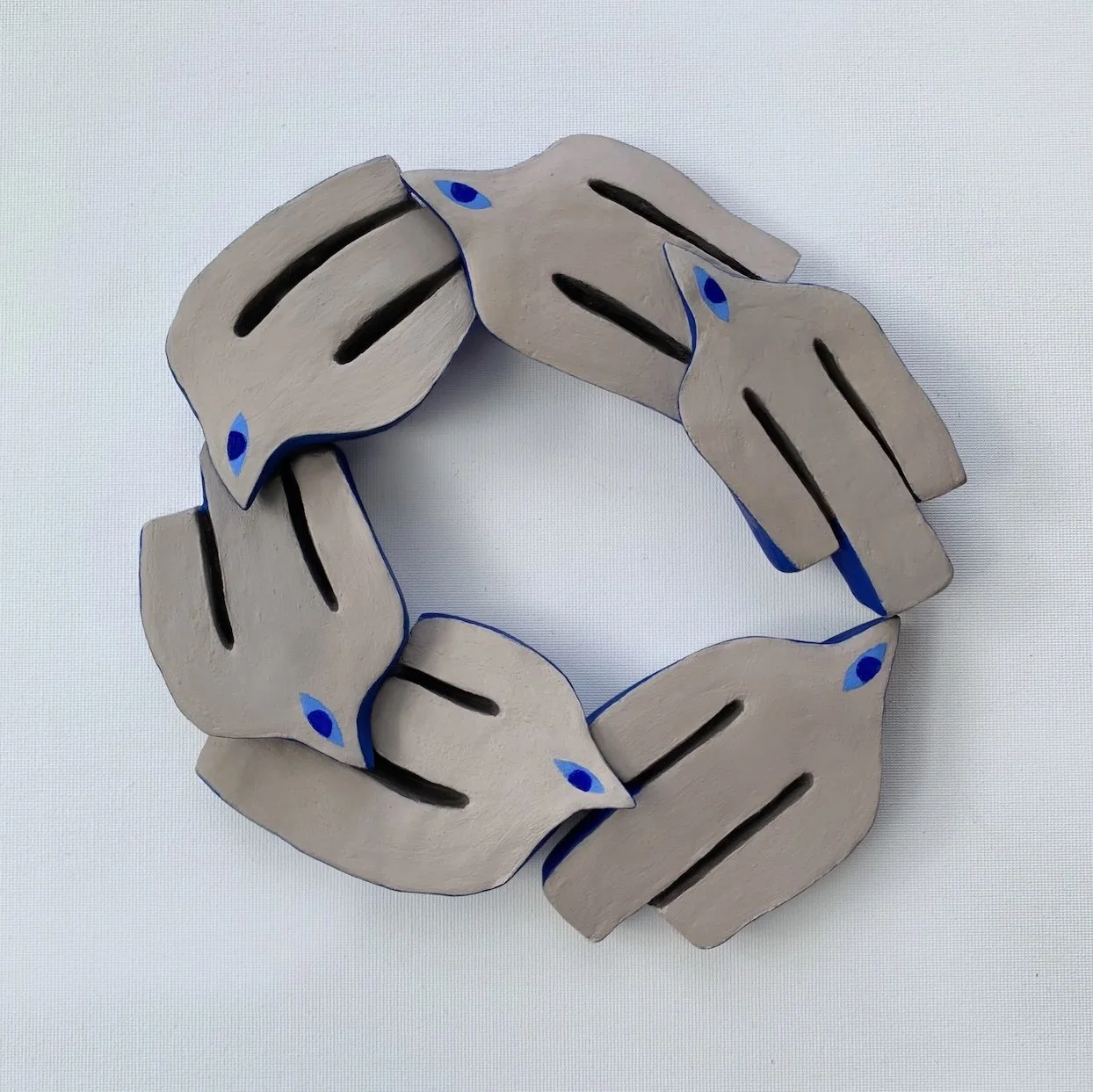 A circular arrangement of six wooden animal sculptures, each resembling a fox, painted in beige with black markings and small blue eyes.