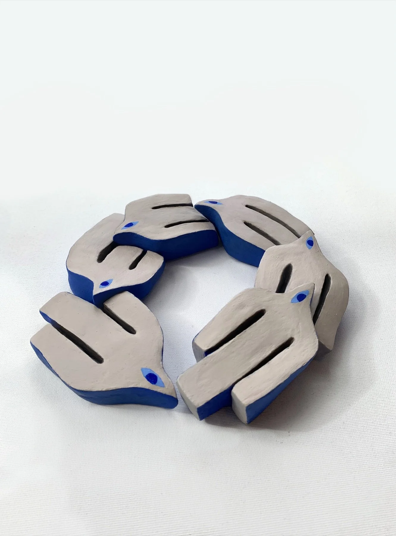 Crafted wooden ring with sections resembling stylized fox faces painted in beige and blue, arranged in a circular pattern on a white background.