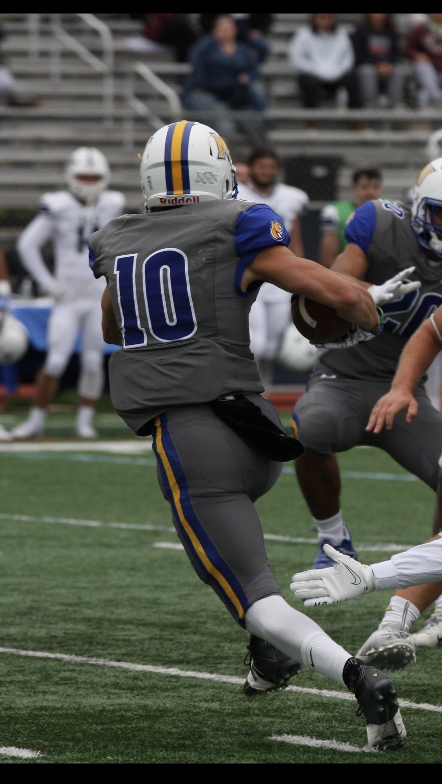 Football player wearing a gray jersey with number 10 and a helmet, running with a football during a game.
